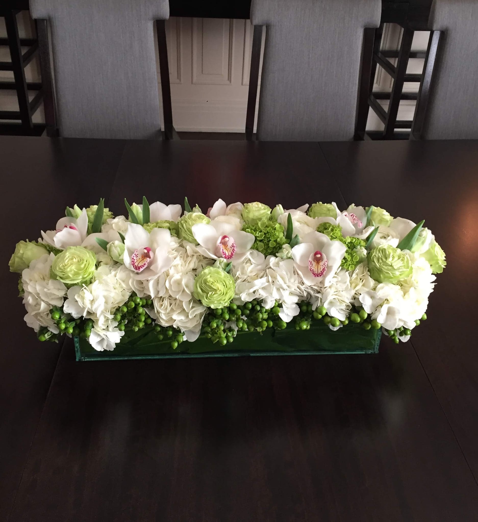 Low rectangular floral arrangement with white orchids, hydrangeas, and green blooms