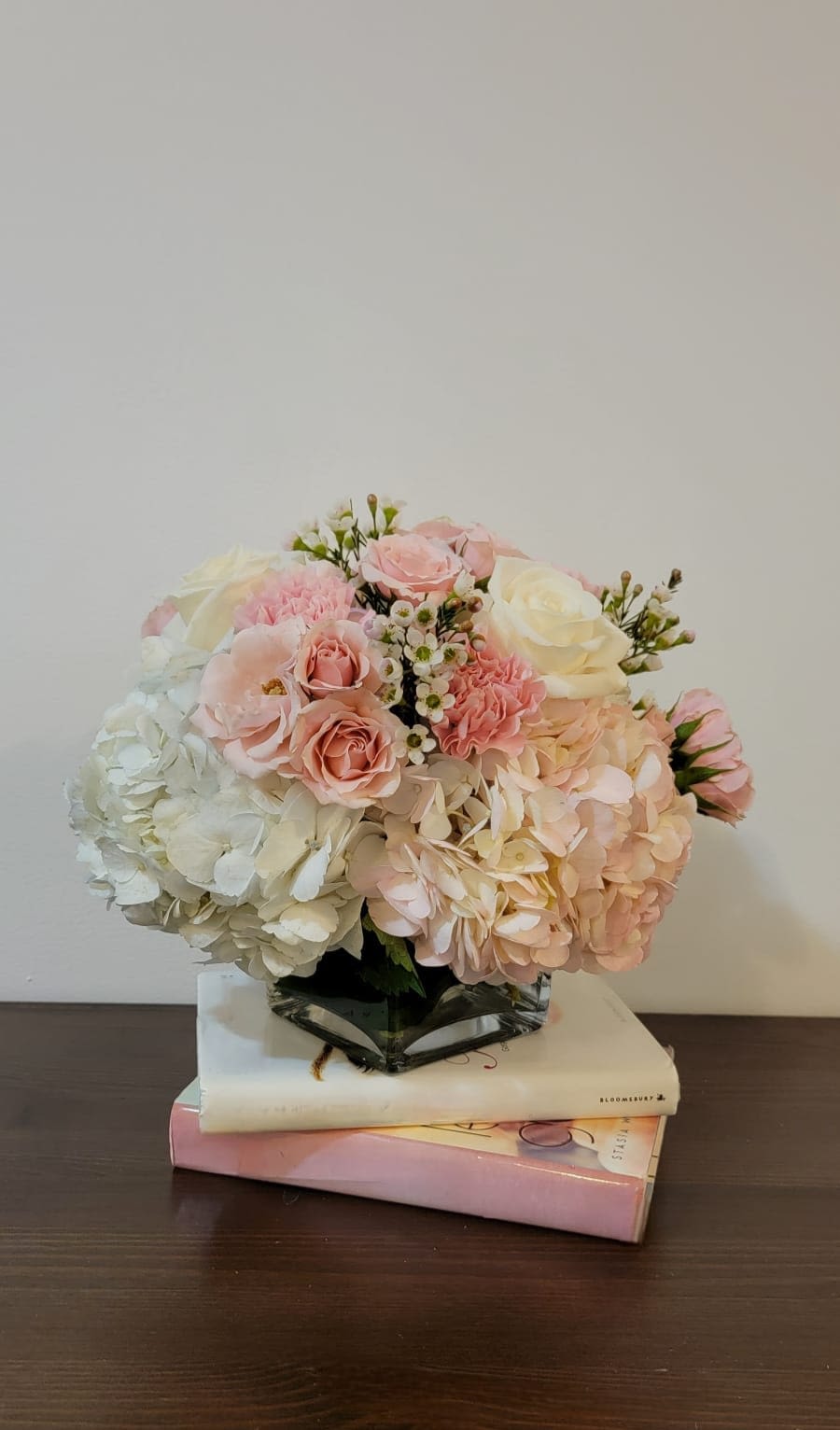 Pink and white floral arrangement in a glass vase on stacked books