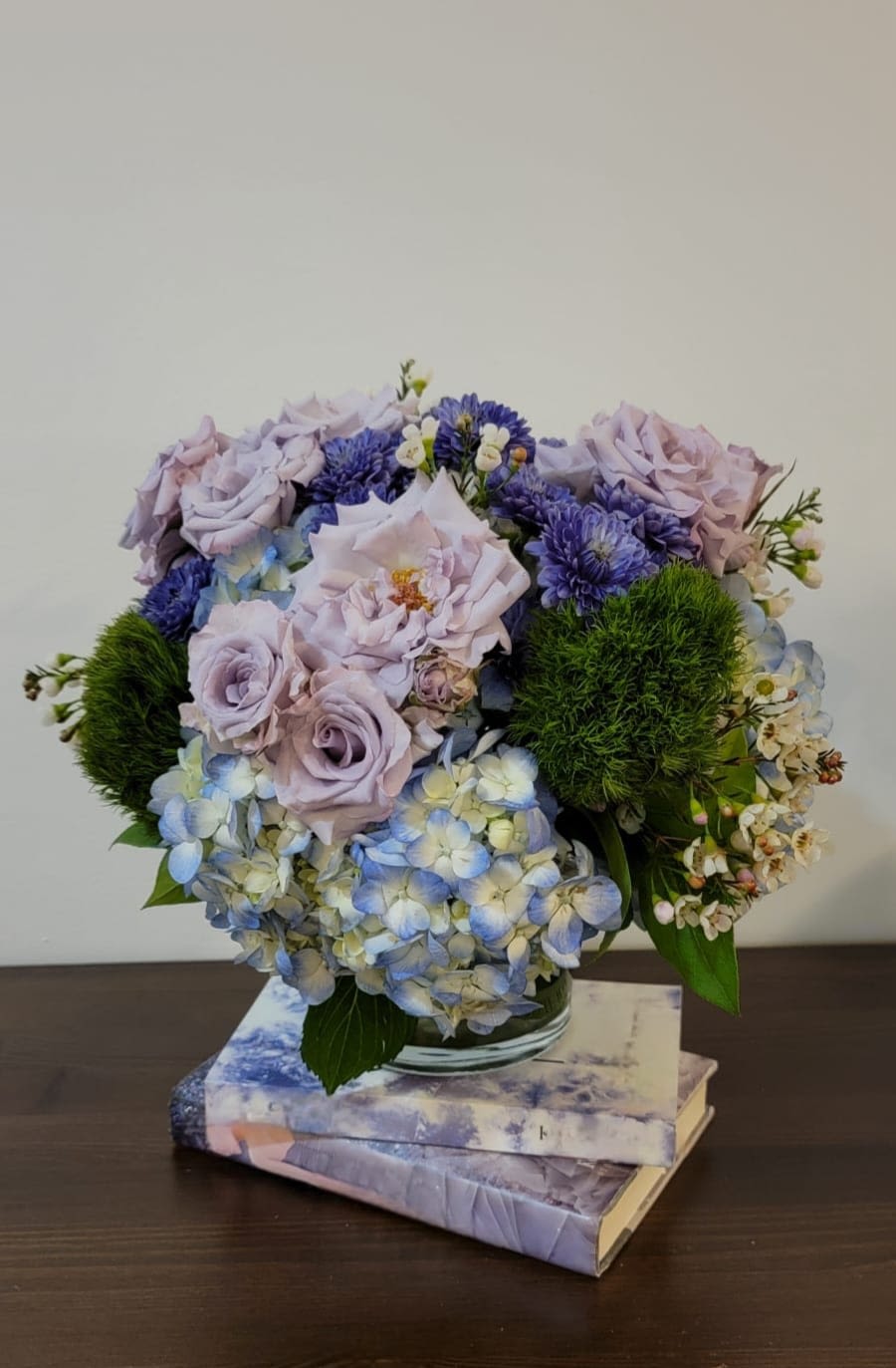 Lavender roses and blue hydrangeas arranged in a glass vase