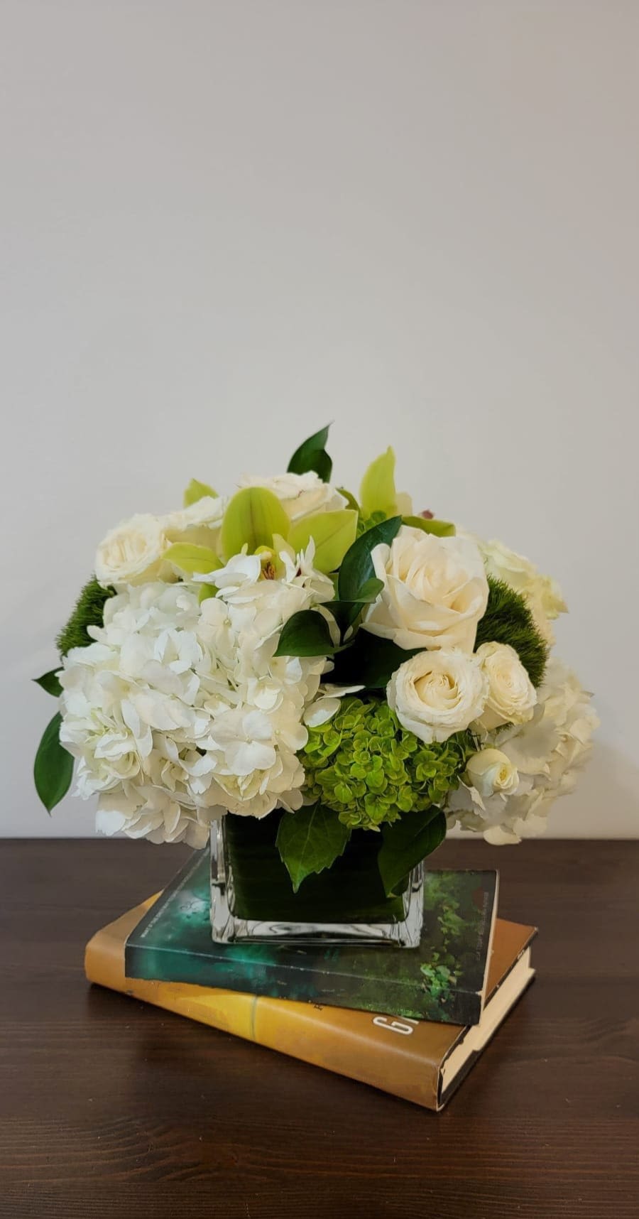 White and green floral arrangement in a square glass vase