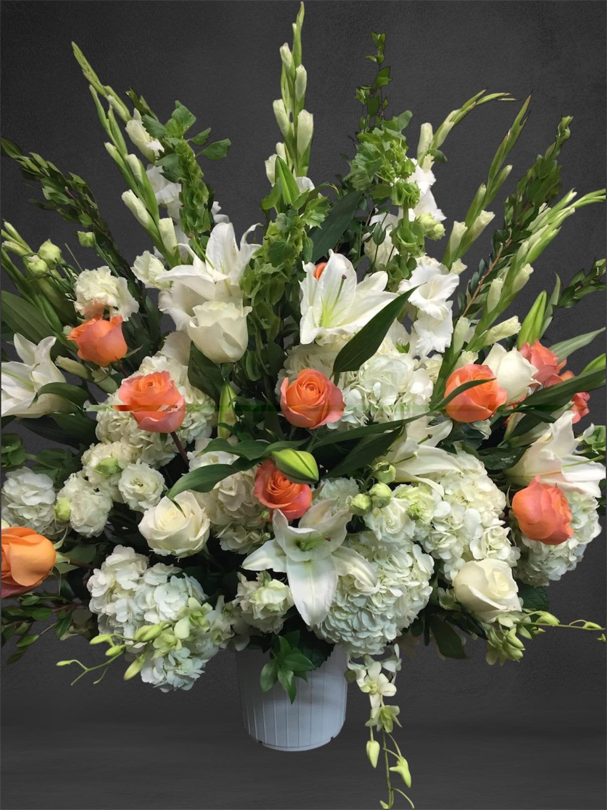 Large white floral arrangement with orange roses in a white vase