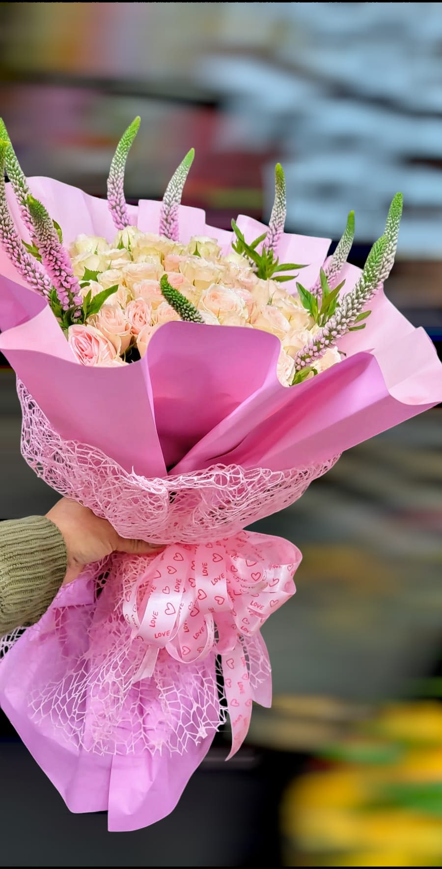 Pink bouquet of pale roses wrapped in pink paper with a heart ribbon
