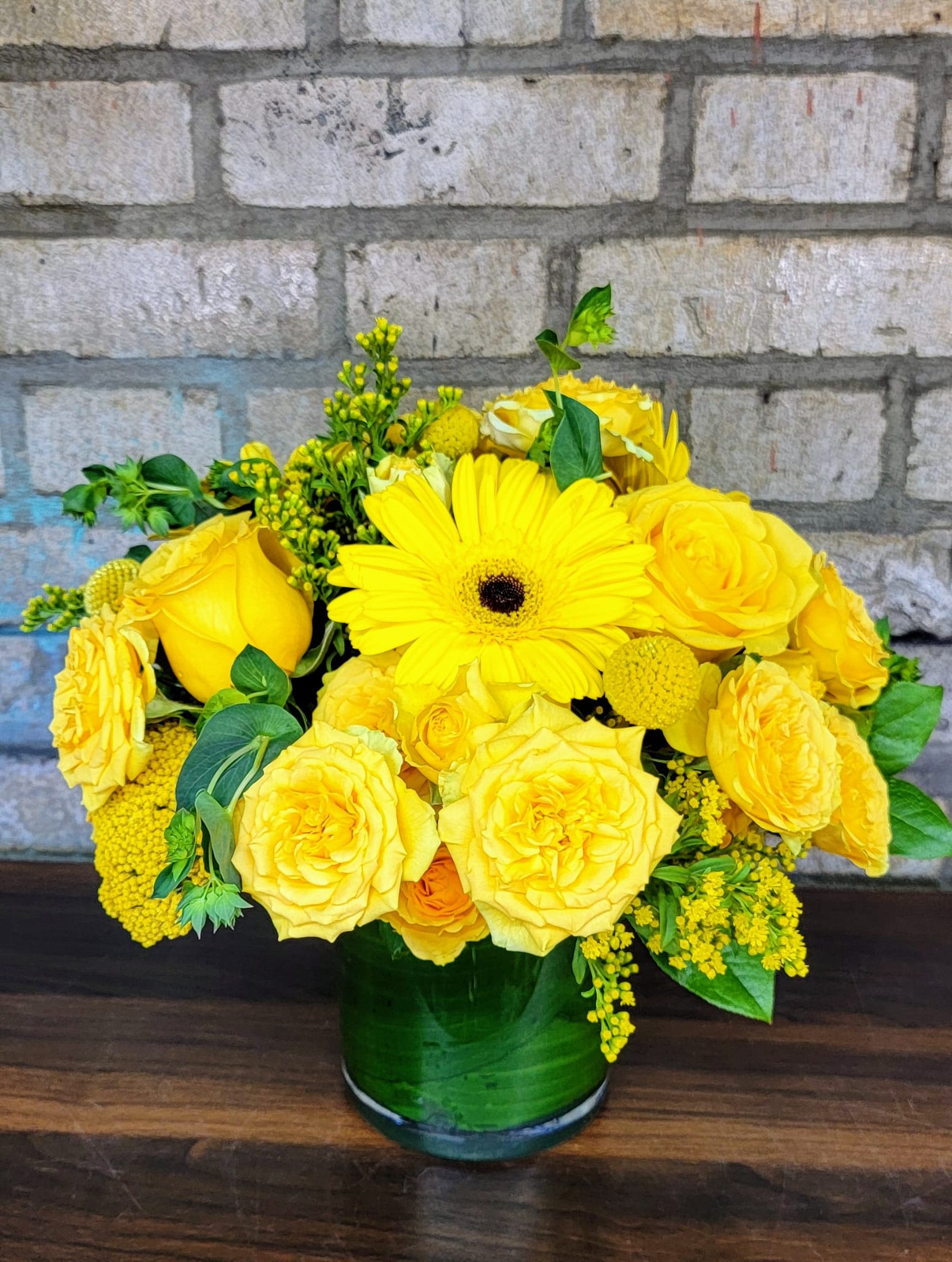 Yellow roses and a gerbera daisy in a green glass vase