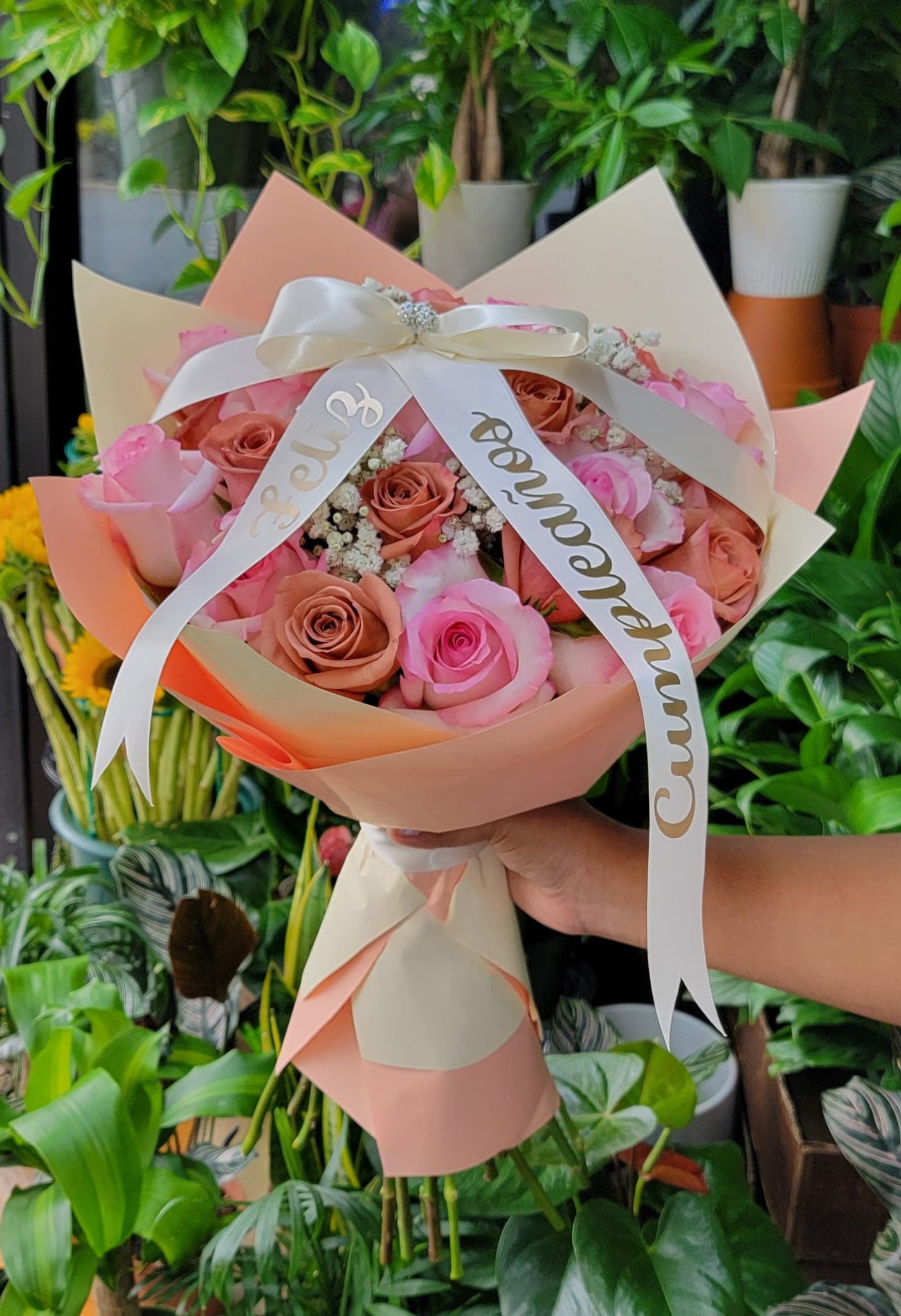 Birthday Babe - This cute wrap bouquet is made up of pink and brown roses with baby breath. Wrapped up in beige and salmon colored paper with a white bow placed on top and on the hanging, ribbon says "Feliz Cumpleanos"