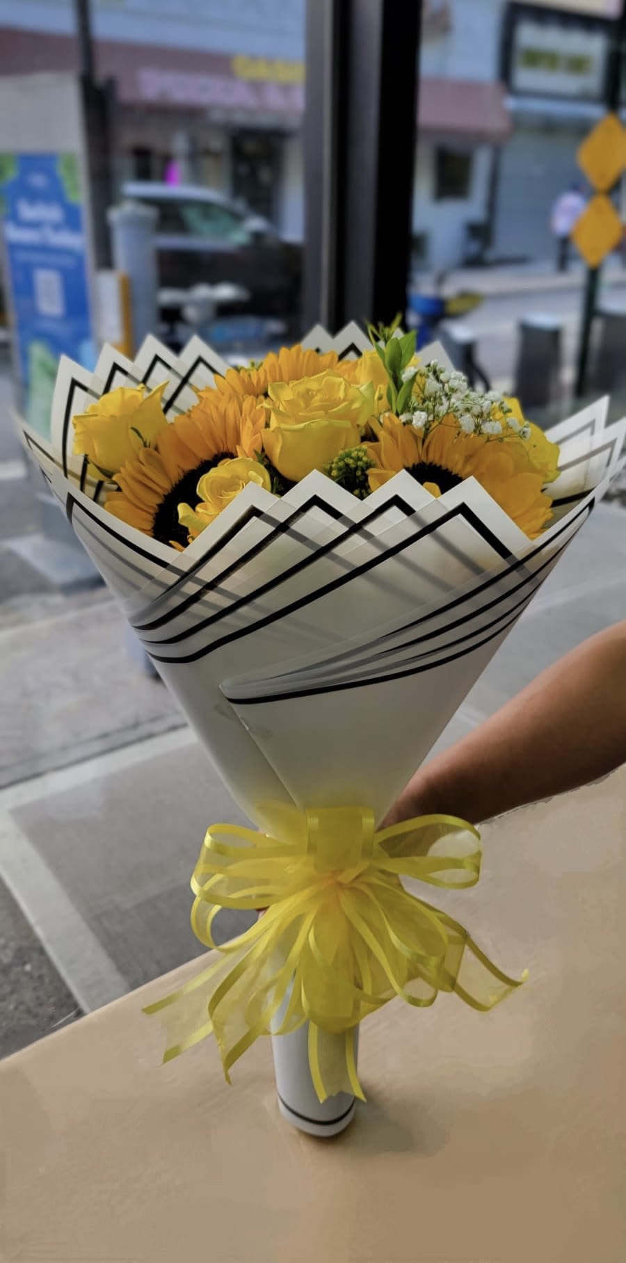 Sweet Sunrise  - This wrap bouquet is made up of yellow roses and sunflowers wrapped in white paper and tied of in a matching yellow bow.