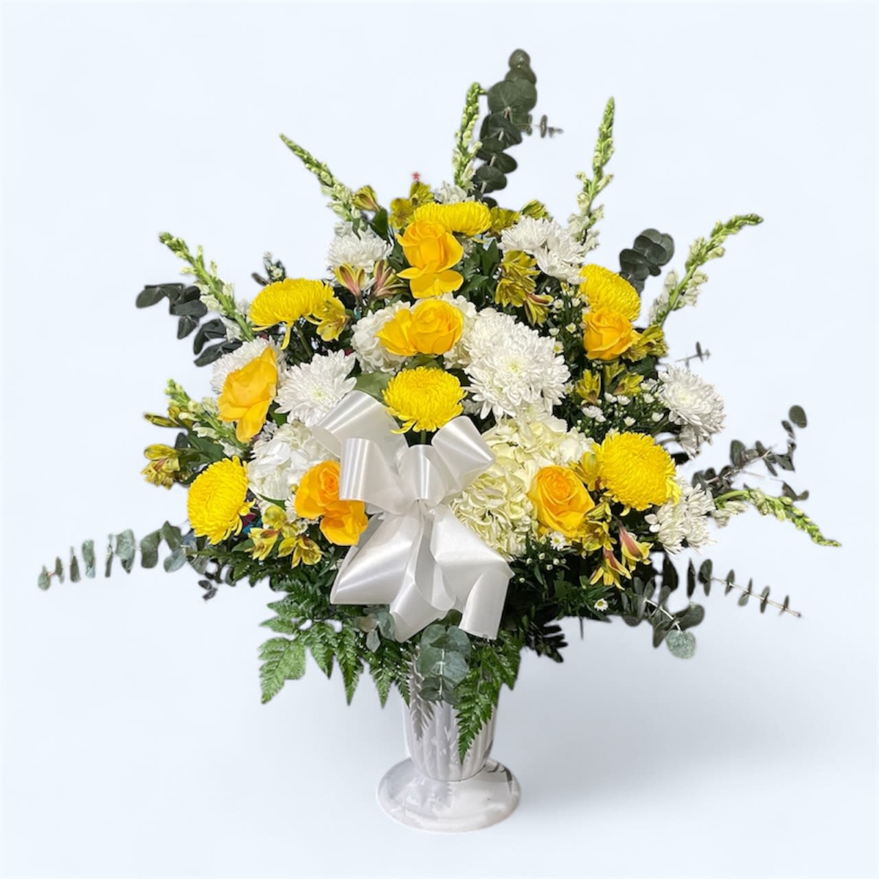 Yellow and white floral arrangement in a silver vase with a white bow