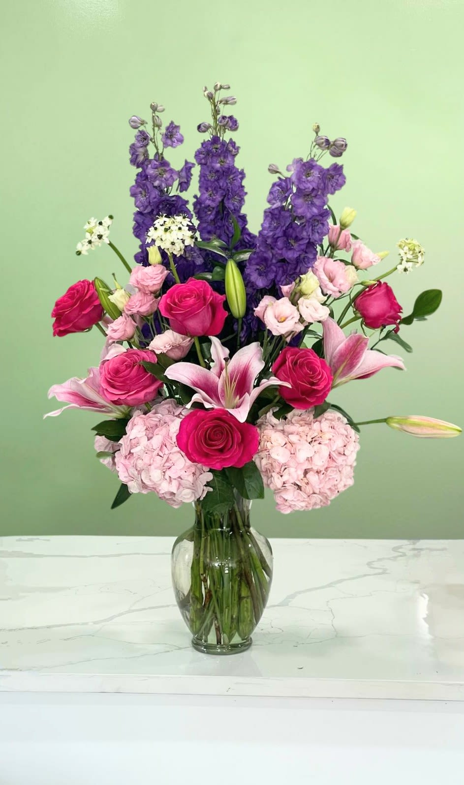 Pink roses and lilies in a glass vase with tall purple blooms