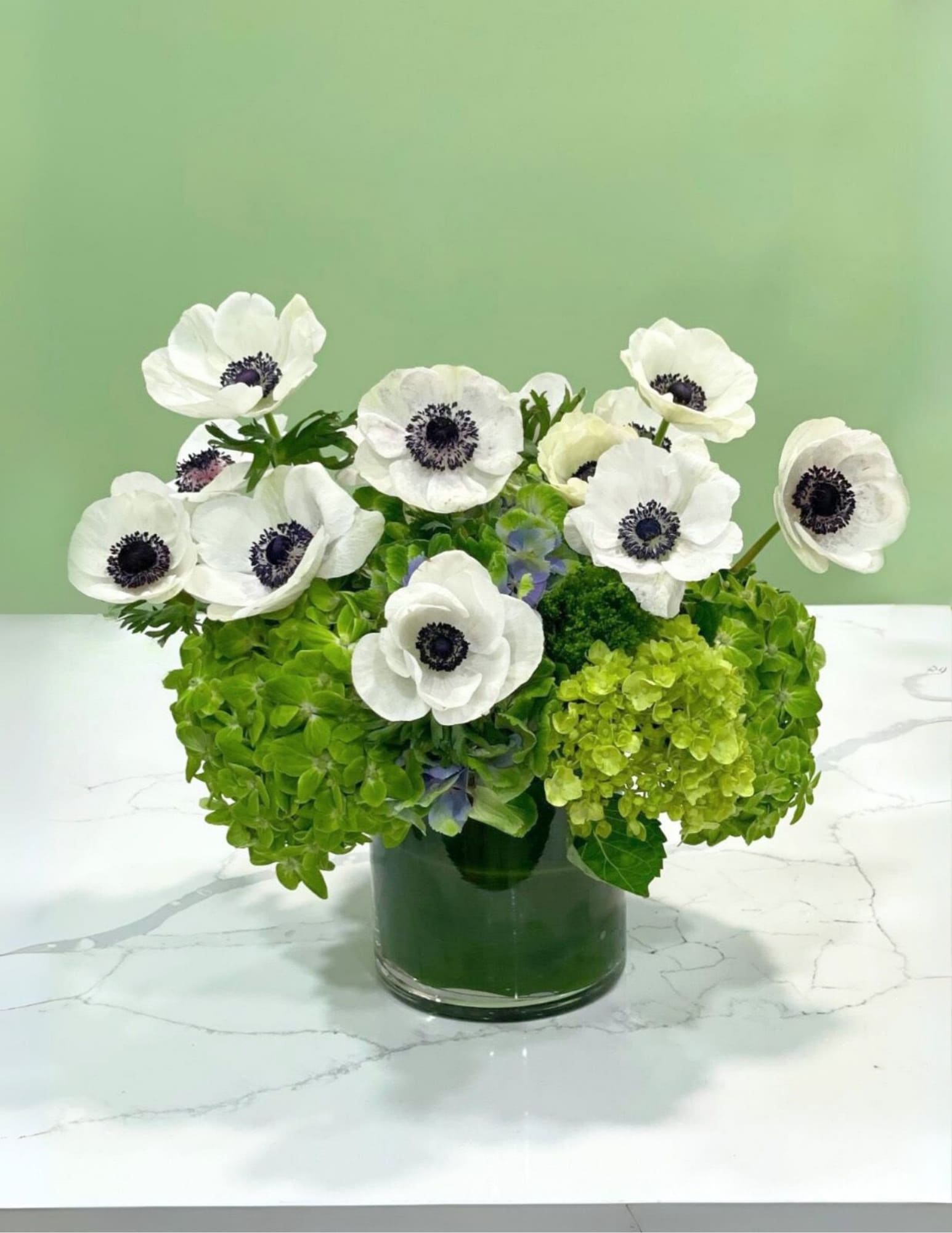 White anemones in a glass vase with bright green hydrangeas