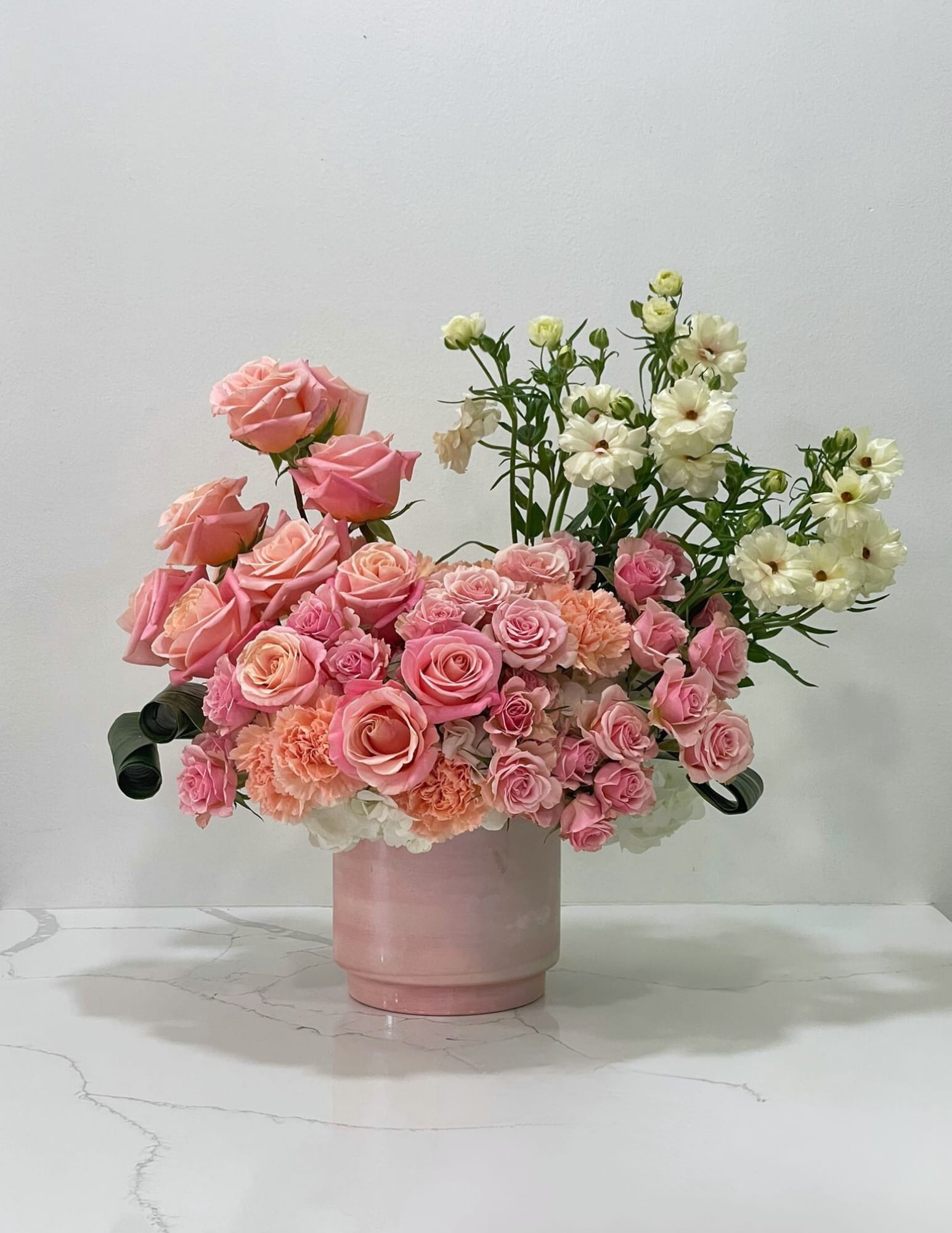 Pink roses and peach carnations in a pink vase with white flowers