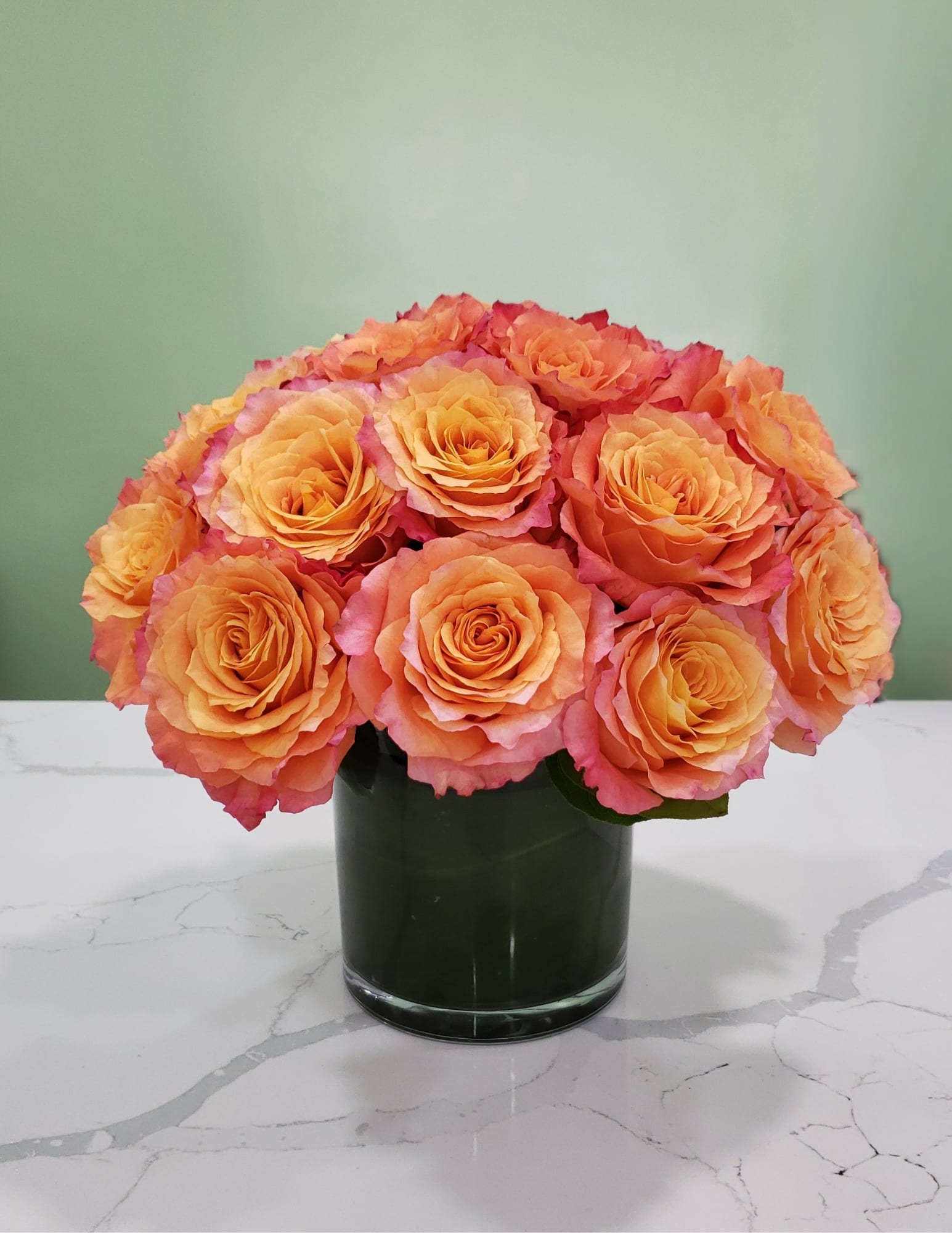 Orange and pink roses arranged in a dark glass vase