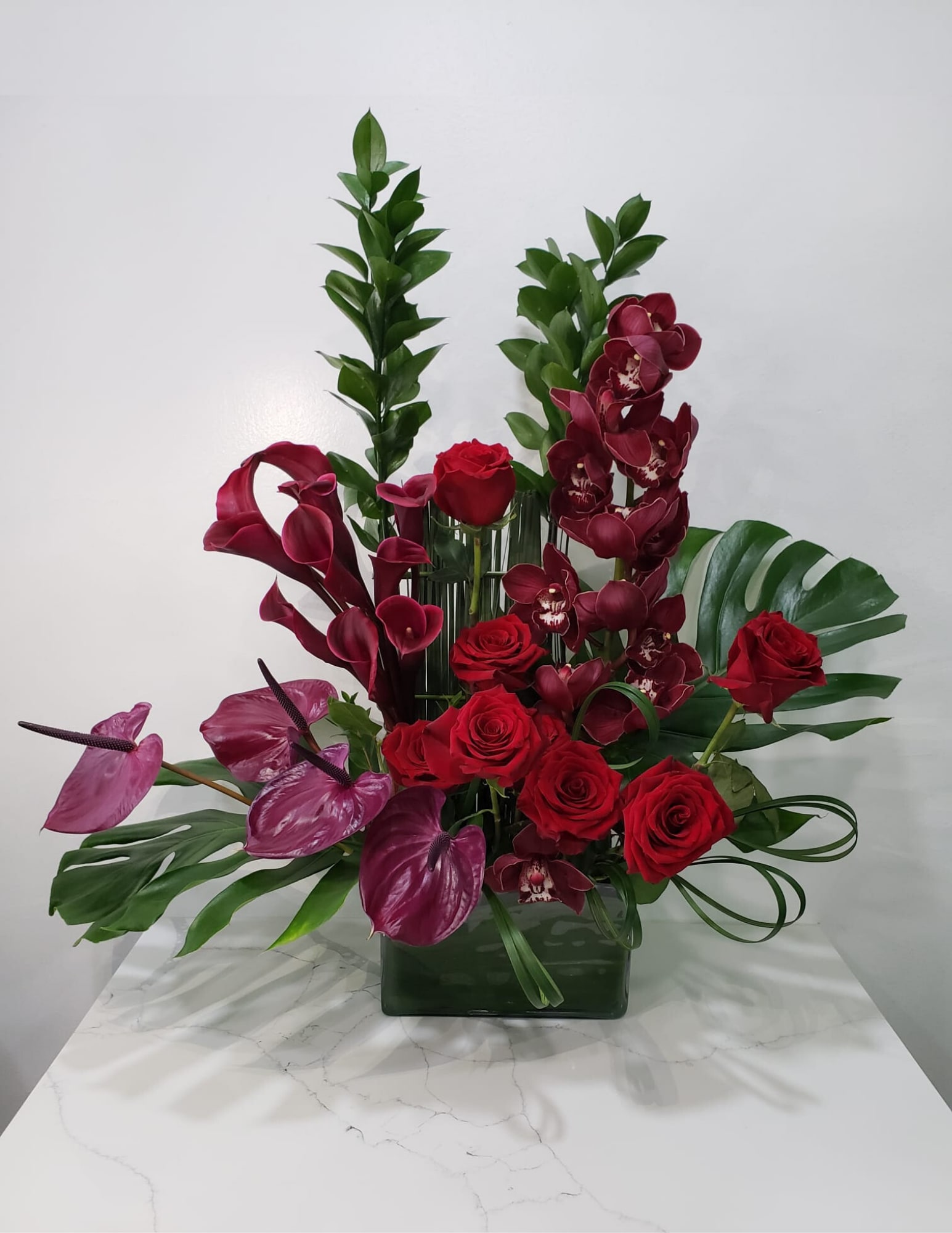Red roses and burgundy orchids arranged in a glass vase