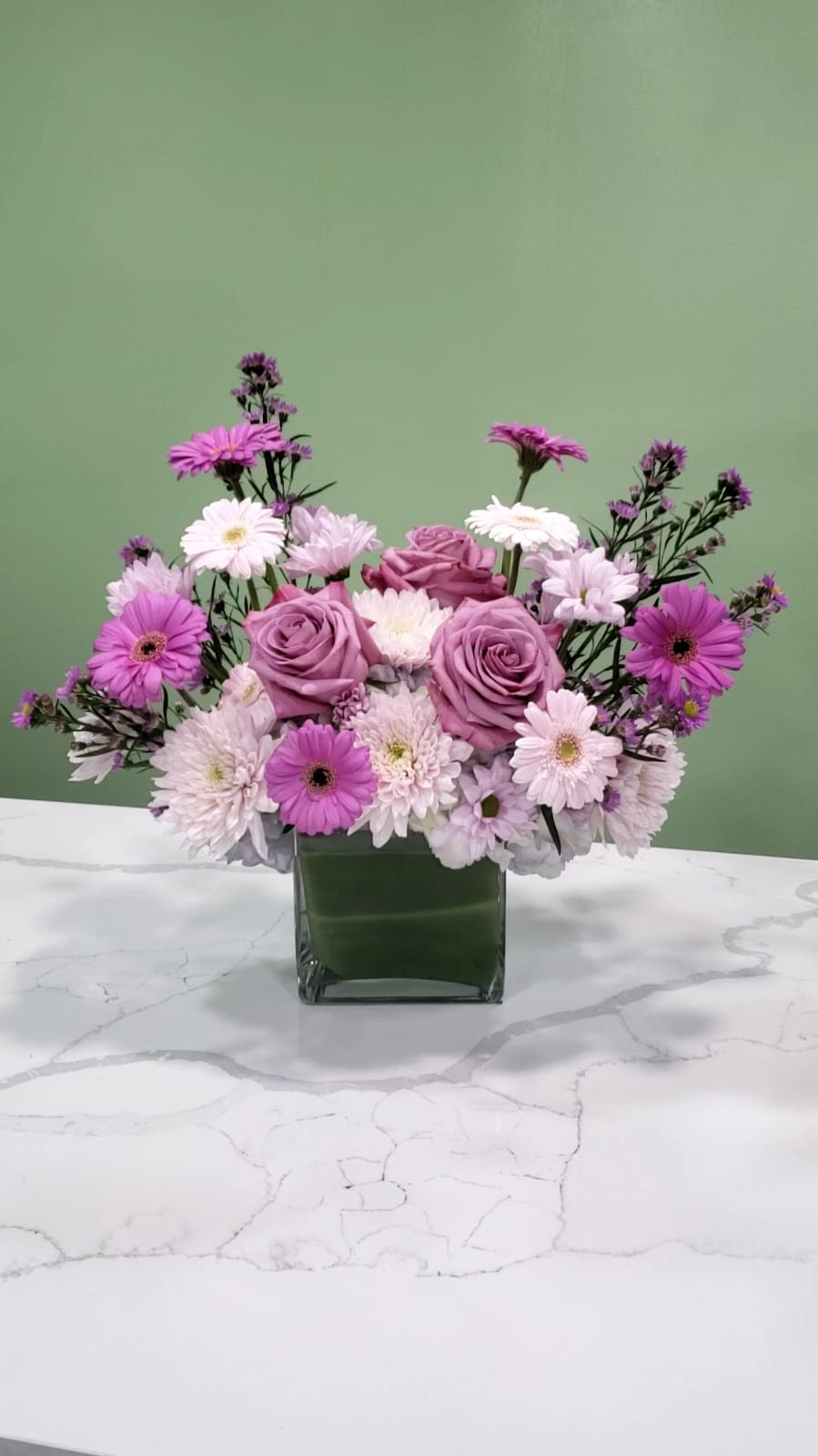 Pink and lavender roses with daisy-like flowers in a square glass vase