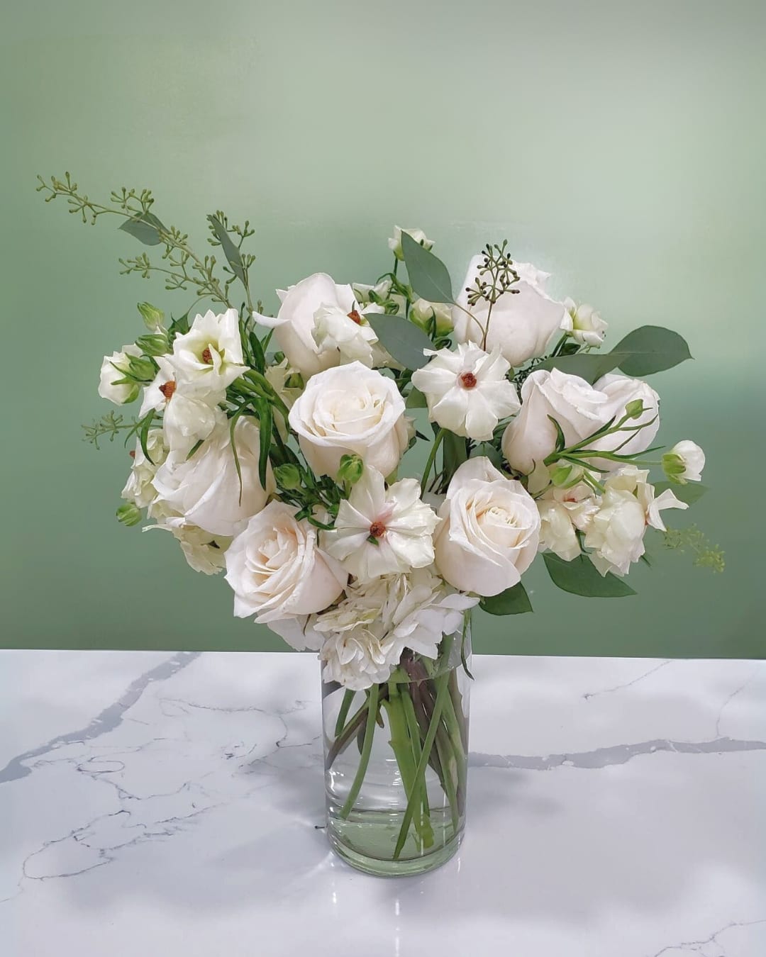 White roses and small white blooms in a clear glass vase