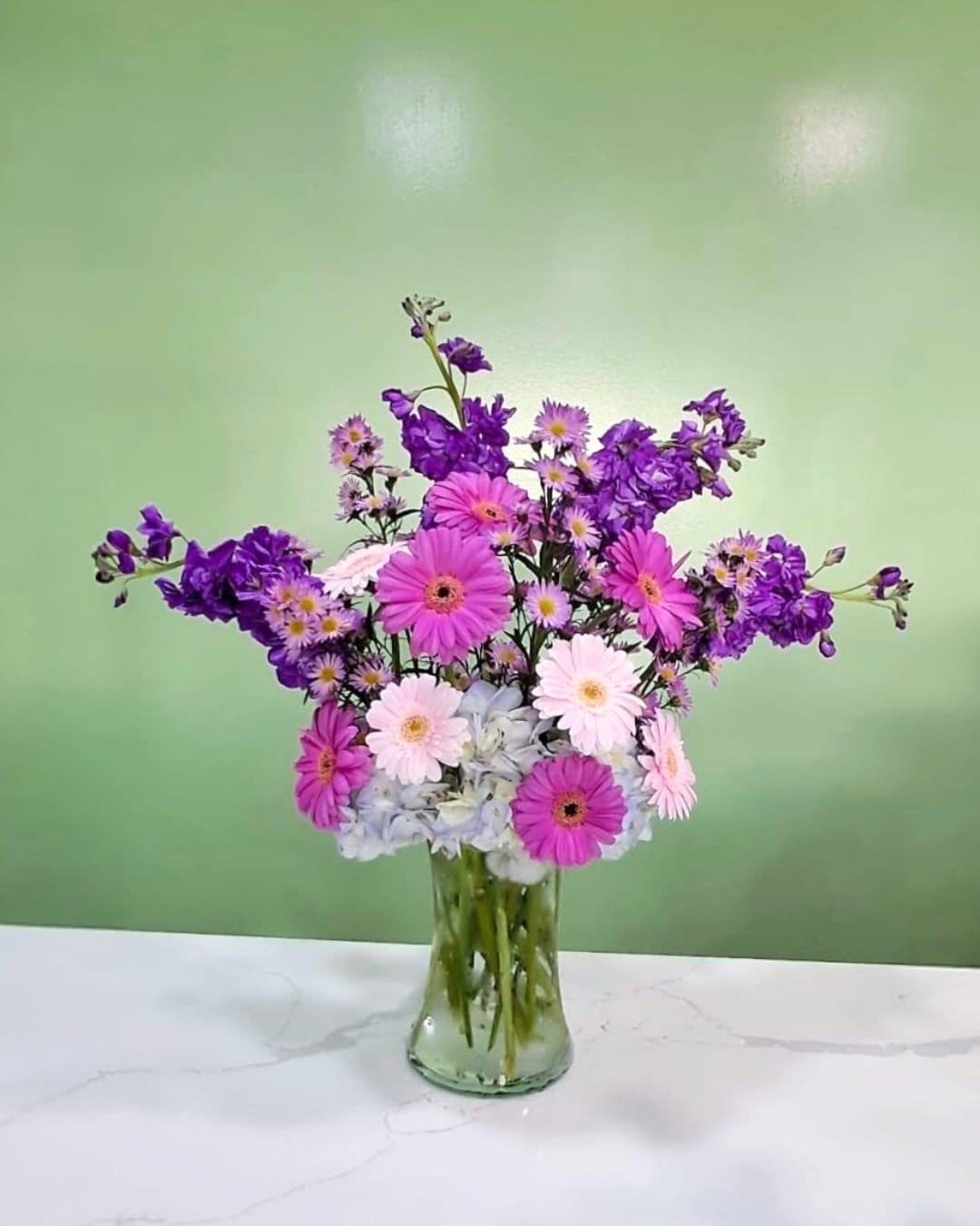 Pink and purple daisy bouquet in a clear glass vase