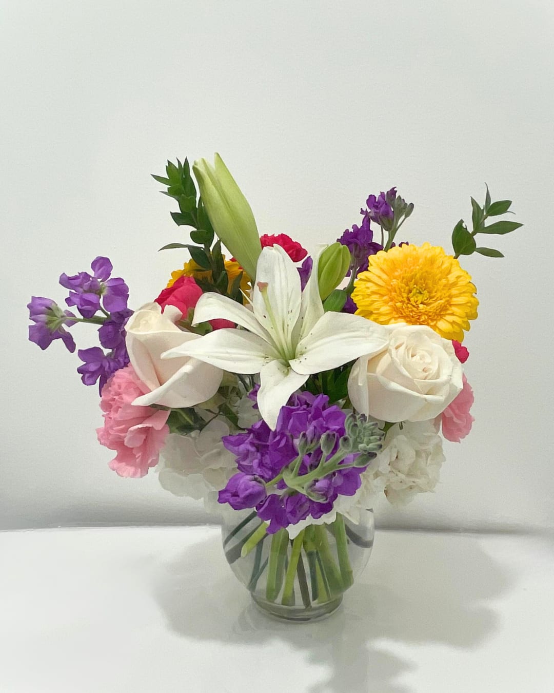 Mixed bouquet in a clear glass vase with white lilies, roses, and purple blooms