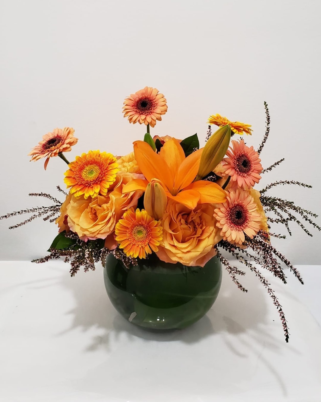 Orange and peach flowers arranged in a green glass vase