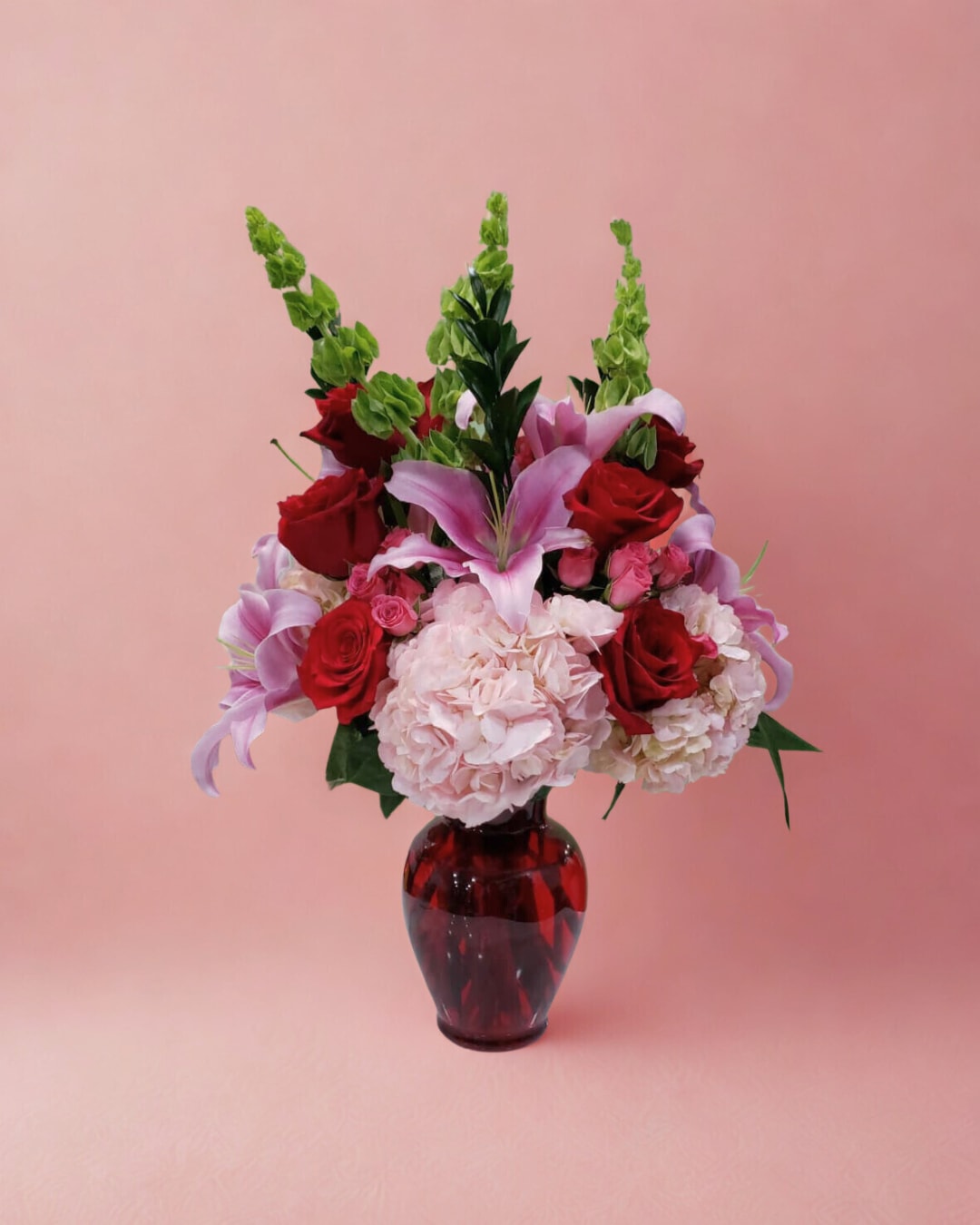 Bouquet of red roses, pink lilies, and pale hydrangeas in a red glass vase
