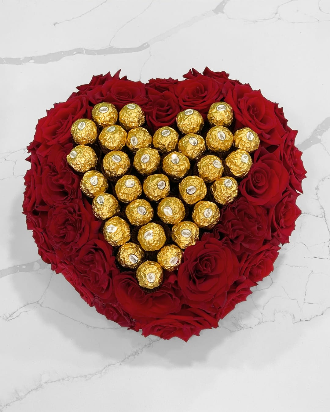 Heart-shaped red rose arrangement with gold-wrapped chocolates in the center