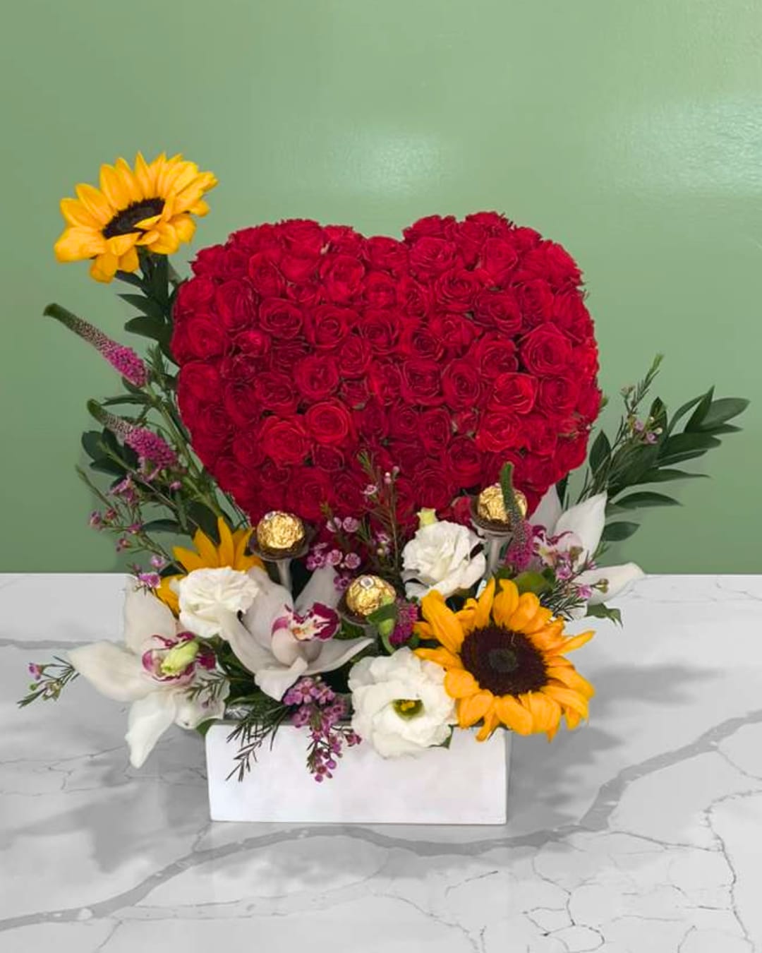 Heart-shaped red rose arrangement with sunflowers and white flowers in a white box