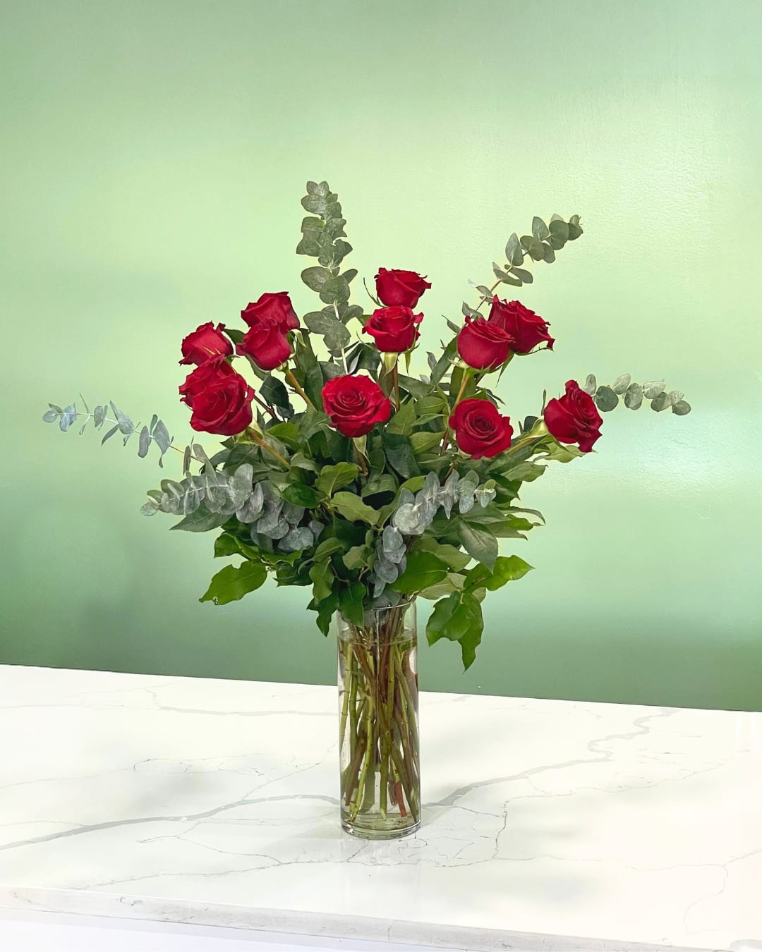 Red roses arranged in a tall glass vase with eucalyptus
