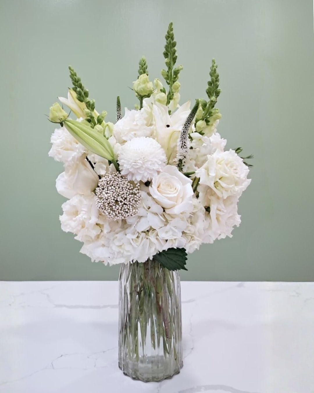 White floral arrangement in a clear glass vase with tall green spikes