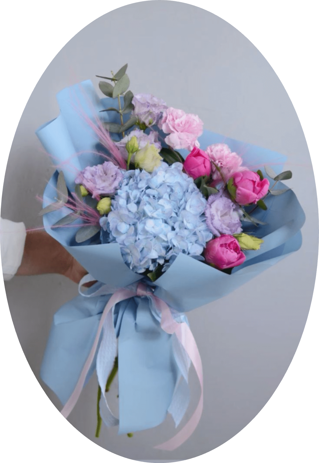 MISS HIDRANGEA ROSES MONTEVIDEO - A pale blue hydrangea anchors this romantic spring bouquet, paired with pink roses and peonies for a soft, celebratory look-perfect as a birthday bouquet, anniversary flowers, or a cheerful baby shower gift. Lavender lisianthus and blush carnations flutter through the arrangement, creating a gentle, airy impression that makes the recipient feel truly seen and celebrated.  Wrapped in layered light-blue paper and tied with a pale pink ribbon, the presentation is as thoughtful as the blooms inside. Eucalyptus-like foliage and wispy pink accent grass add texture and a hint of green without stealing the pastel spotlight. Choose this bouquet to send warmth and tenderness; its delicate colors and lush blooms arrive ready to display and enjoy.