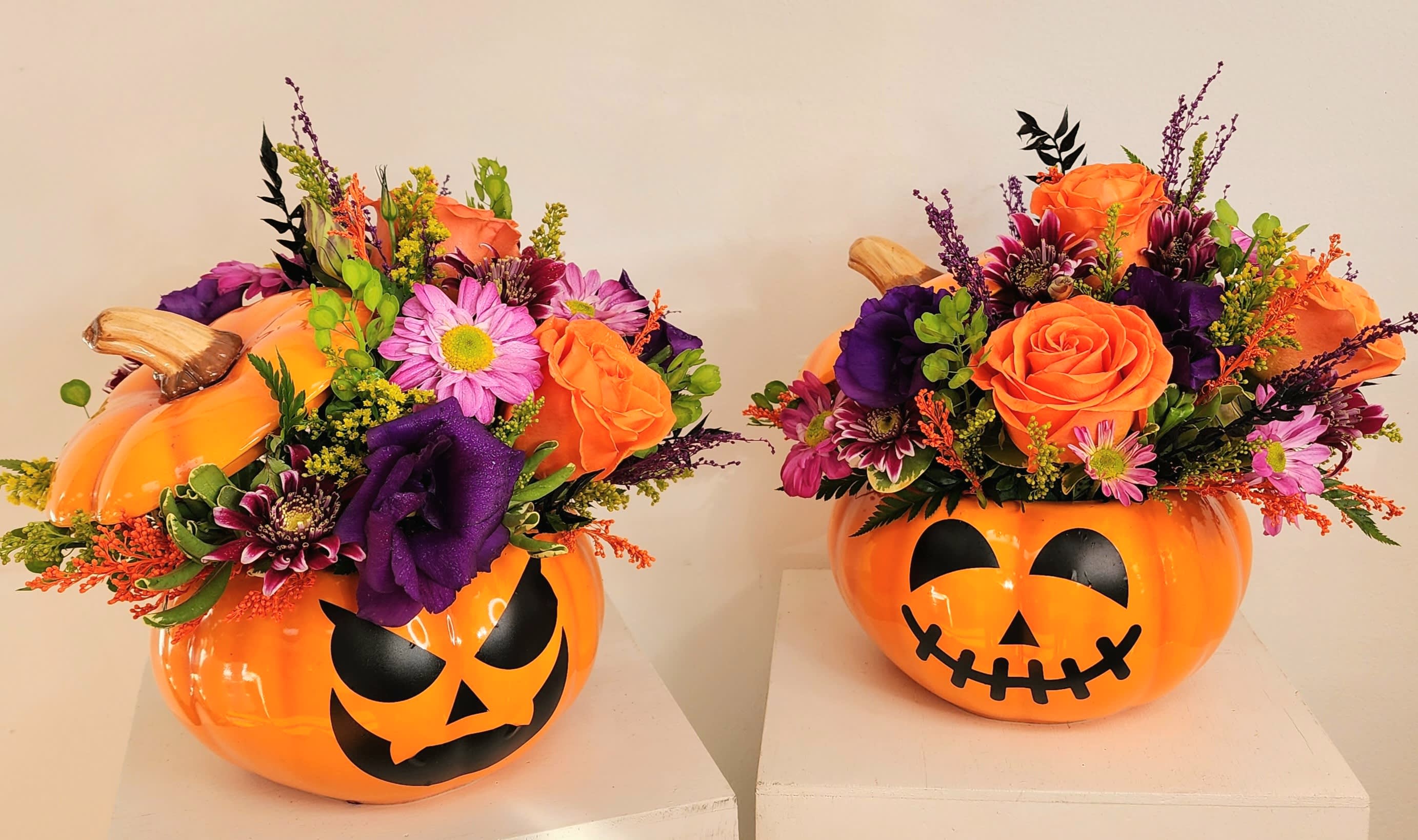 Two orange jack-o'-lantern containers filled with mixed flowers