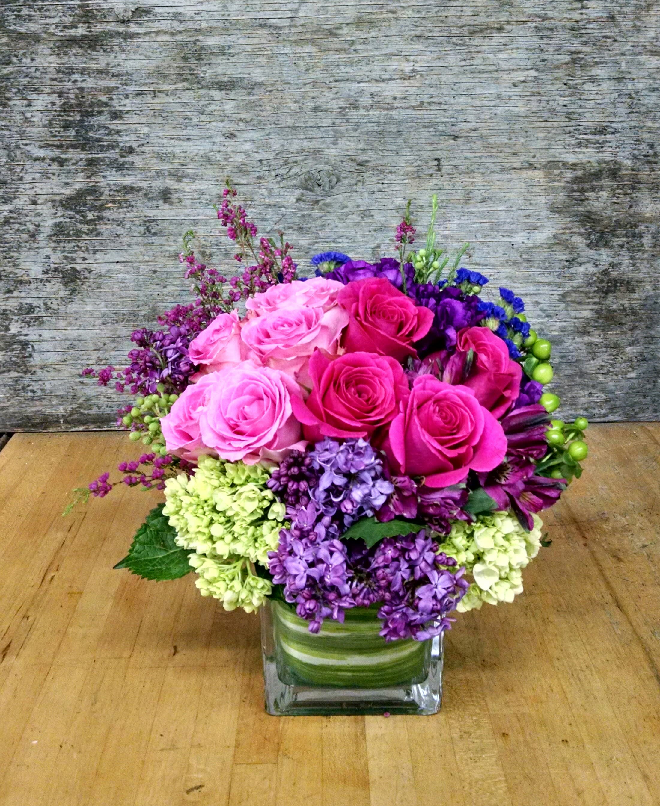 Pink and purple rose arrangement in a square glass vase