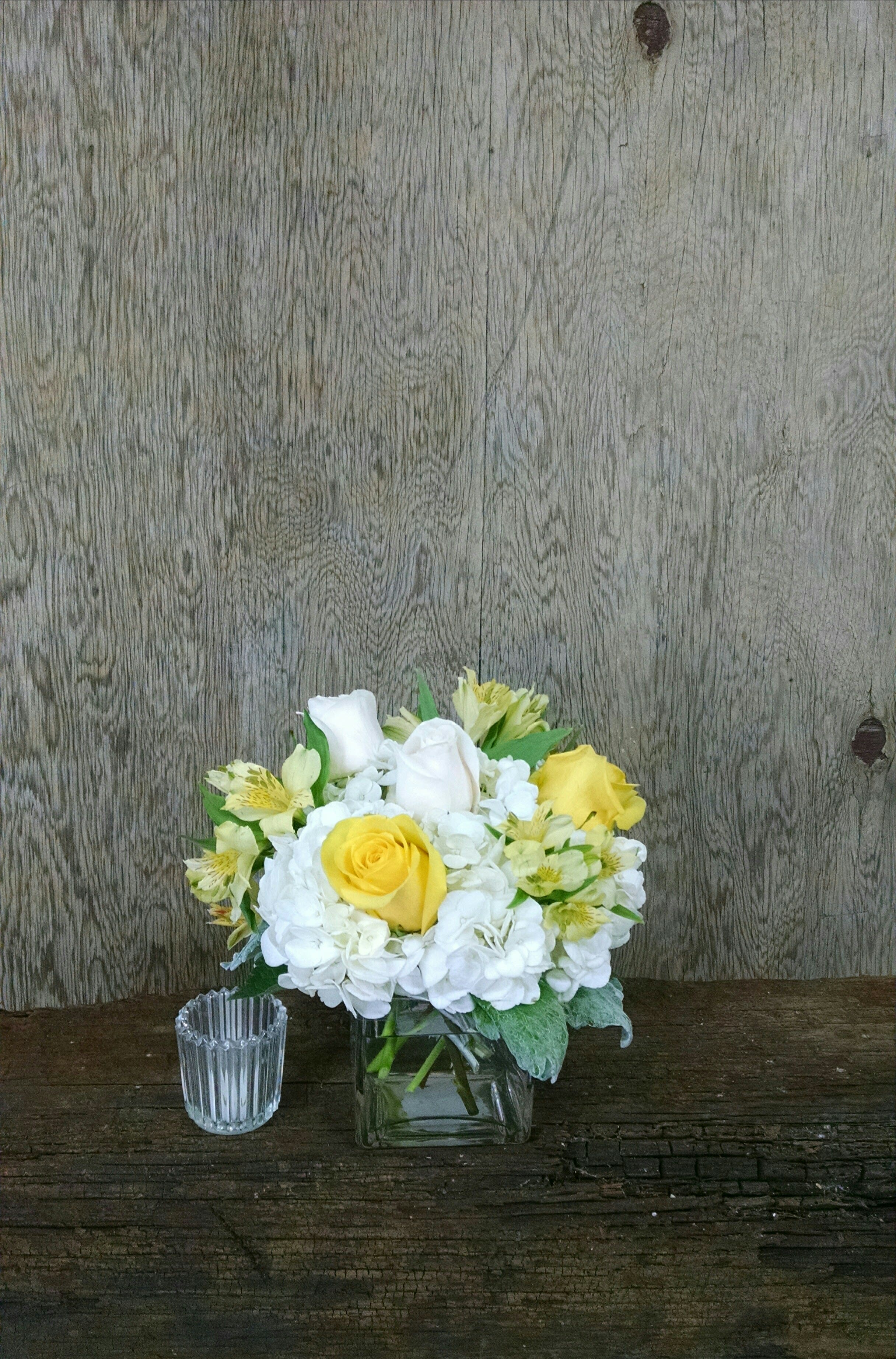 Yellow and white roses in a square glass vase with white hydrangeas