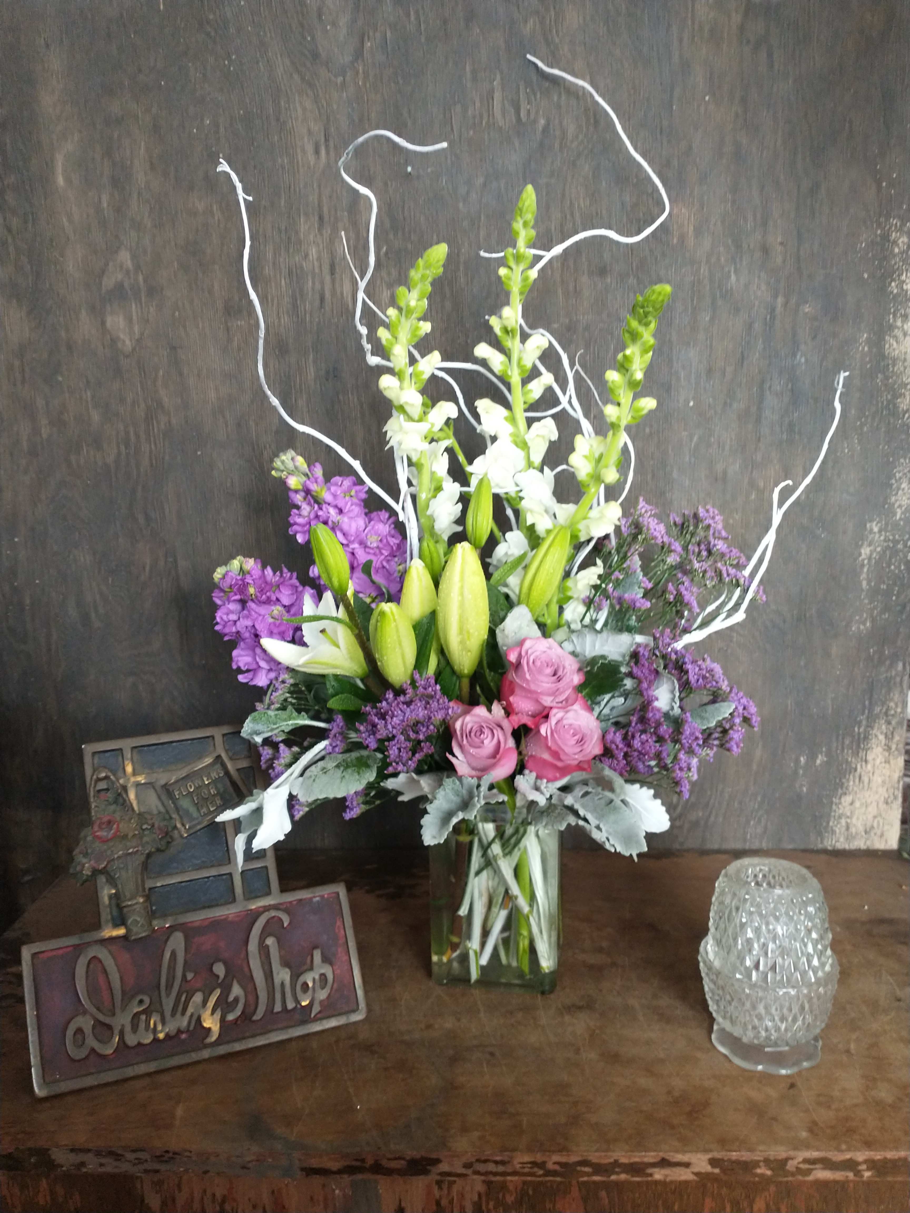 Tall bouquet of lilies, roses, and purple flowers in a glass vase