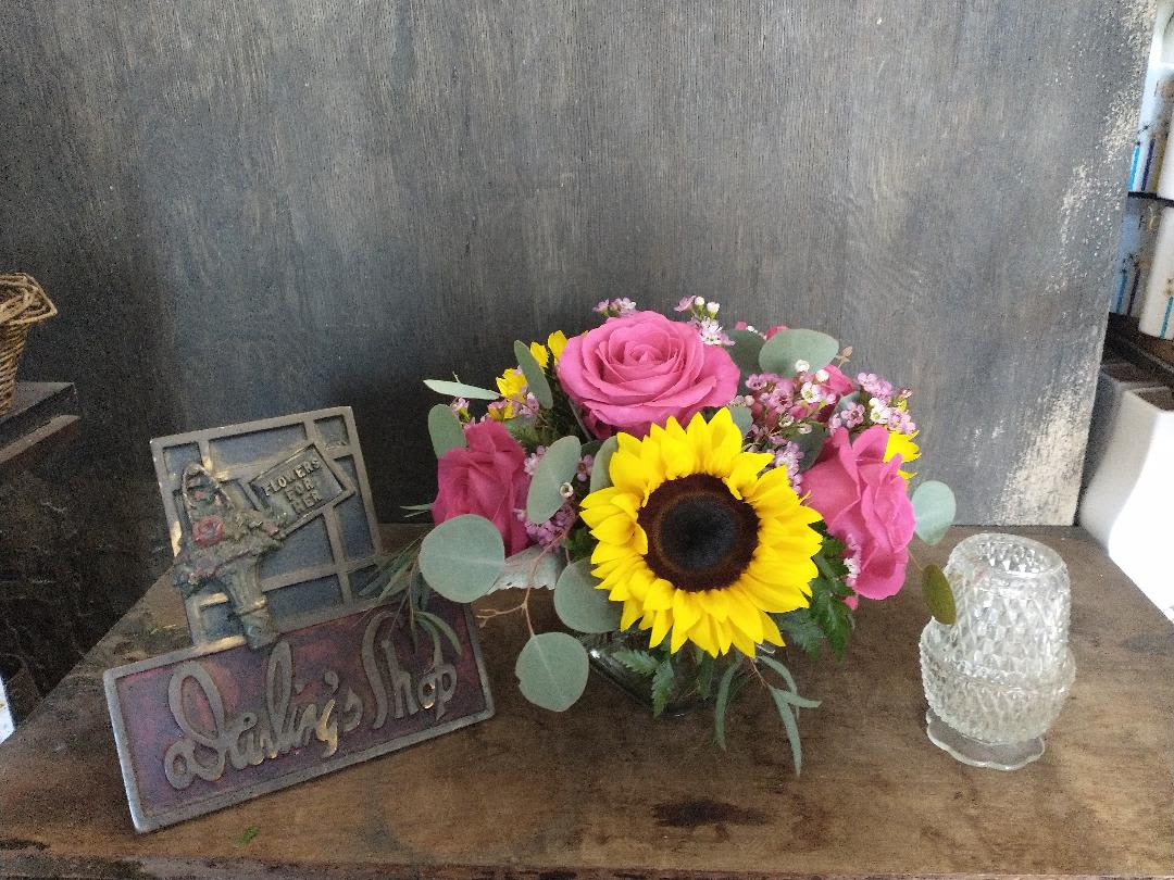 Pink roses and a sunflower in a low glass vase with small filler flowers