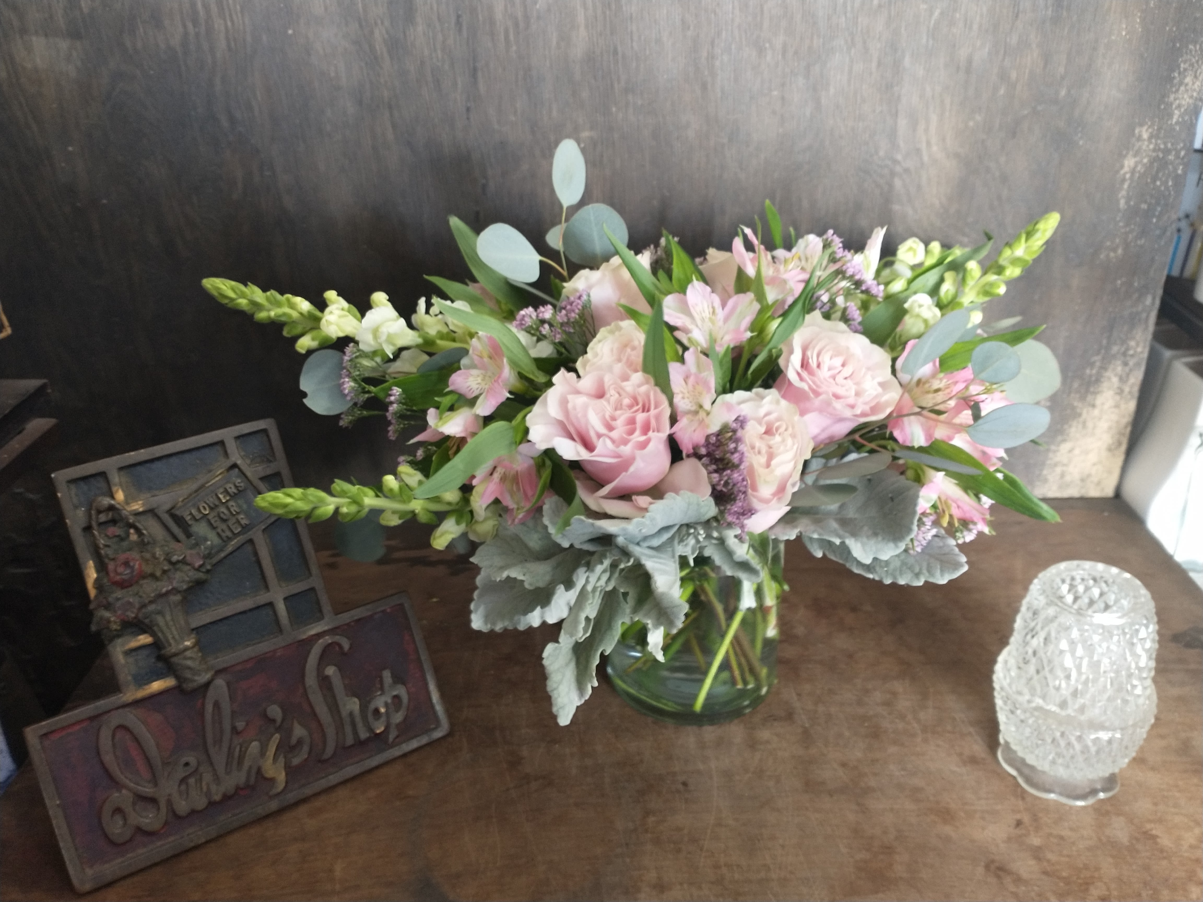 Low glass vase of pink carnations, alstroemeria, and white snapdragons with soft gray foliage.