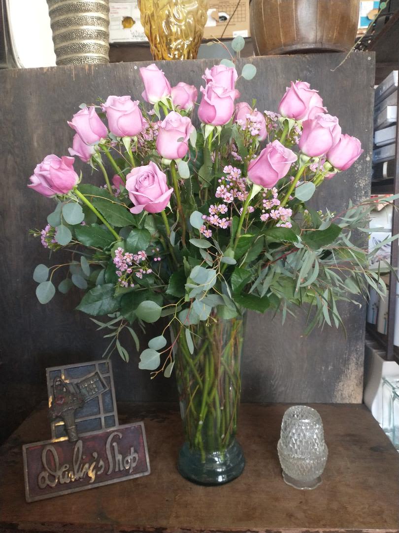 Pink roses arranged in a tall glass vase with eucalyptus and small filler flowers.