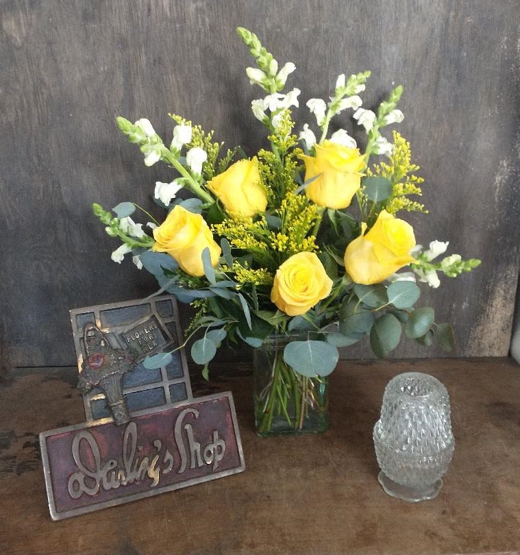 Yellow roses in a glass vase with white snapdragons and a small glass candle holder