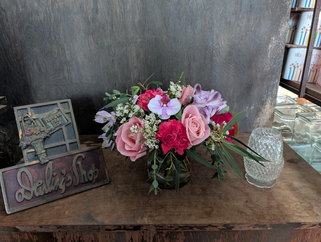 Pink and lavender flower arrangement in a glass vase on a wooden table