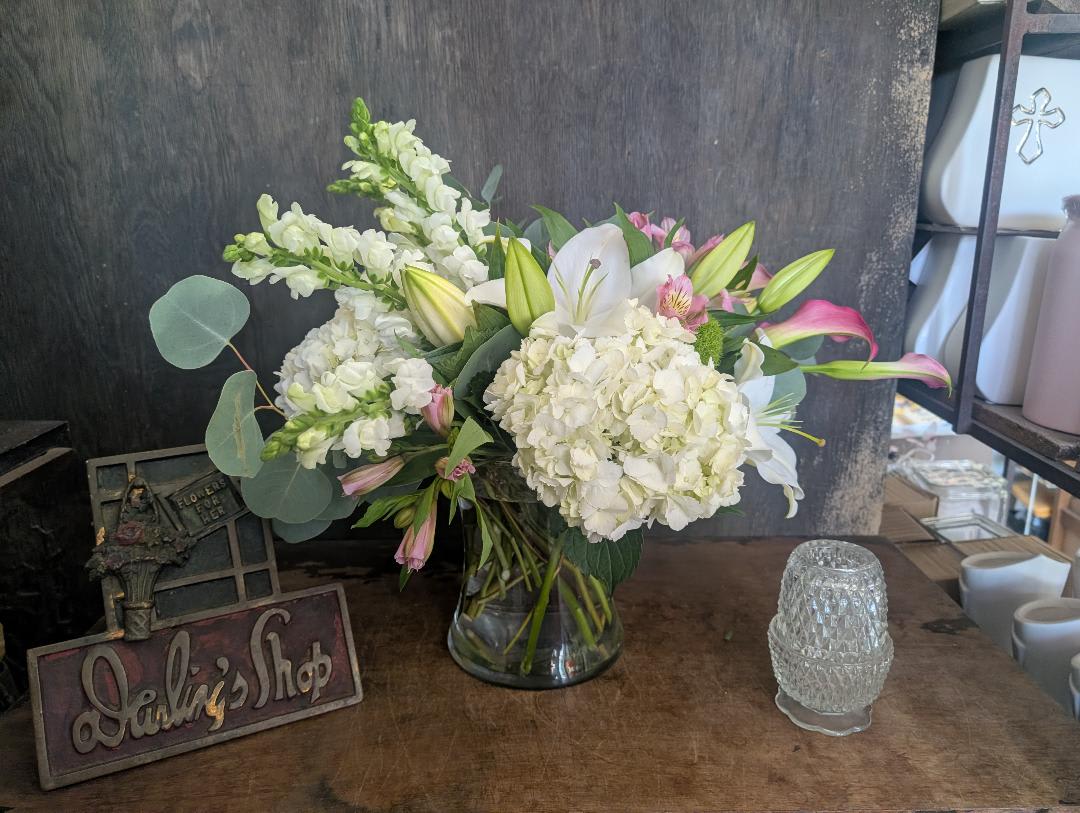 White lilies and hydrangeas in a glass vase with pink accents