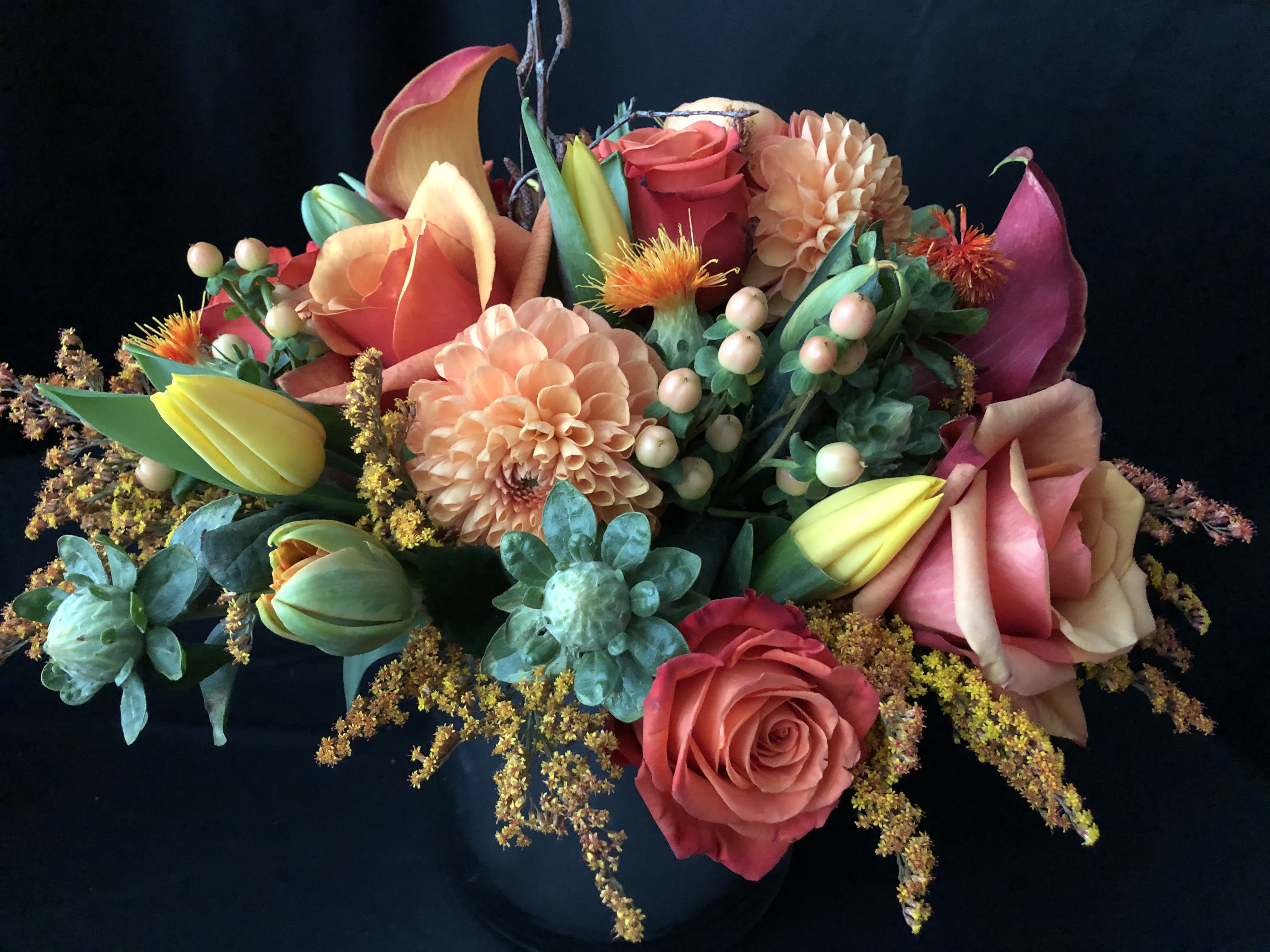 Mixed bouquet with roses, calla lilies, dahlias, and tulips in a dark vase
