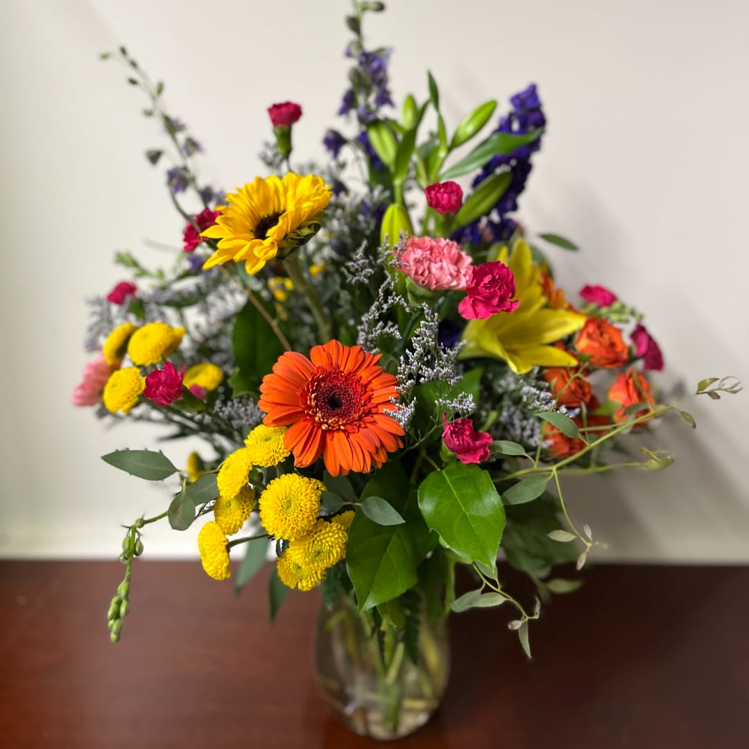 Mixed bouquet with sunflowers, gerbera daisies, and colorful blooms in a glass vase
