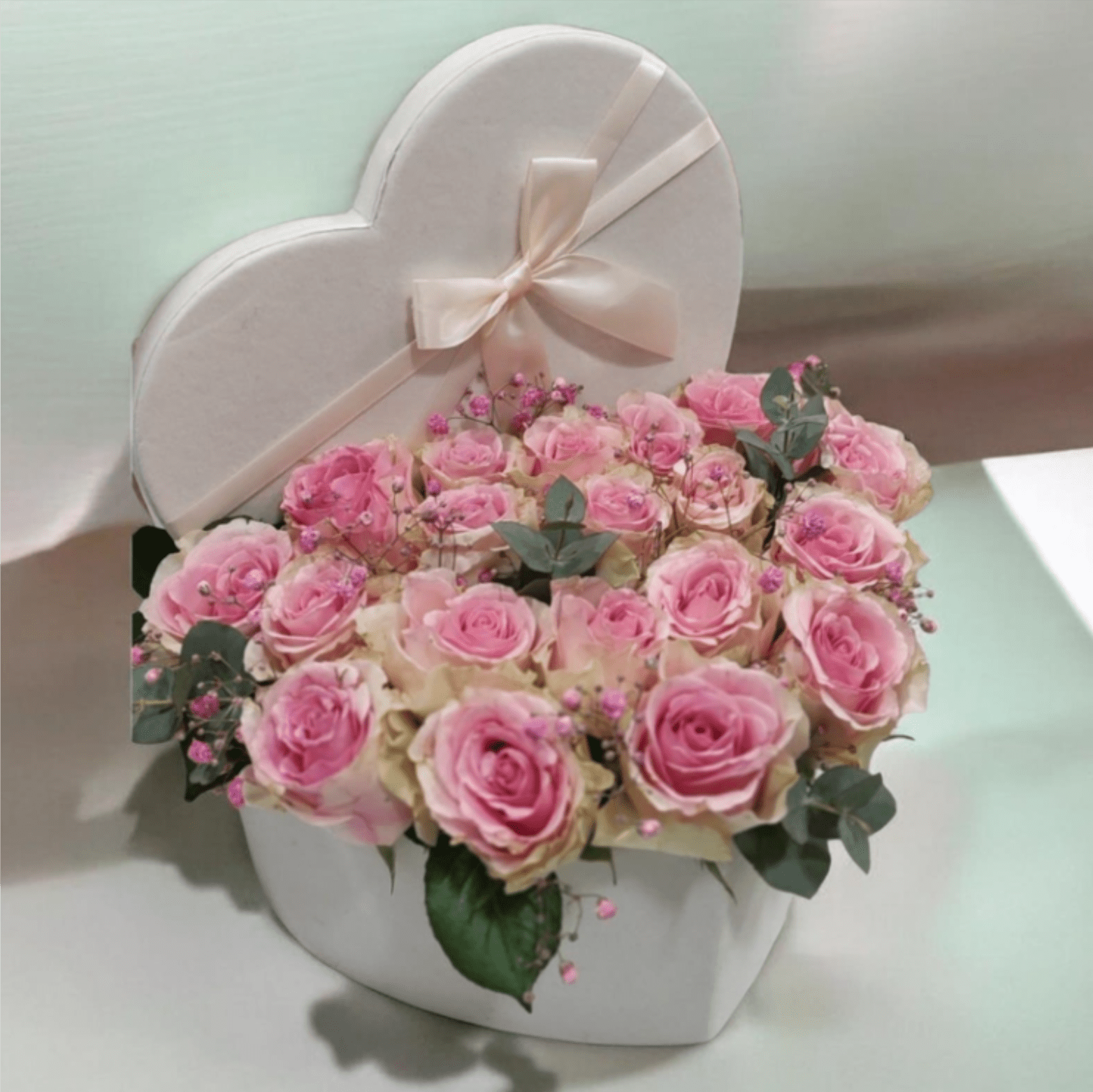COLONIA   HEART BOX WITH ROSES - A cloud of white hydrangeas and layered ranunculus softens with scattered pink roses and ruffled carnations in this romantic hand-tied flower arrangement-perfect as a birthday bouquet, anniversary flowers, or a thoughtful "I'm thinking of you" gift. The airy white-and-pink palette reads feminine and celebratory, so the person you send it to will feel cherished and noticed the moment it arrives.  The design pairs full white hydrangea heads with delicate pink ranunculus, pink roses, and carnation-like blooms for a lush, textured look set against touches of green foliage. Finished in white paper wrap and tied with a long pink ribbon, the bouquet arrives gift-ready; select the heart-shaped box option to present the same soft pink roses in a white heart box with a pale satin bow for a distinctly romantic presentation ideal for anniversaries or Valentine's Day.