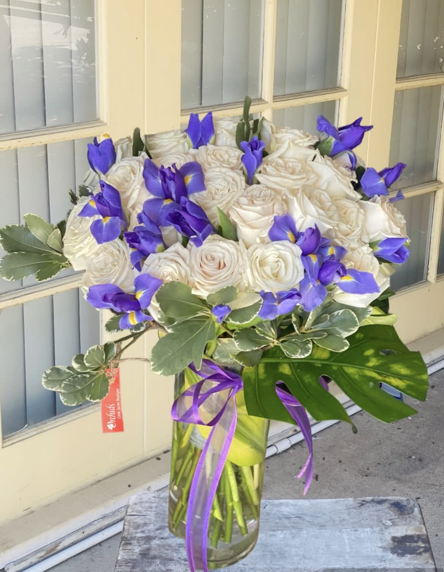 White roses and purple irises in a glass vase with a ribbon