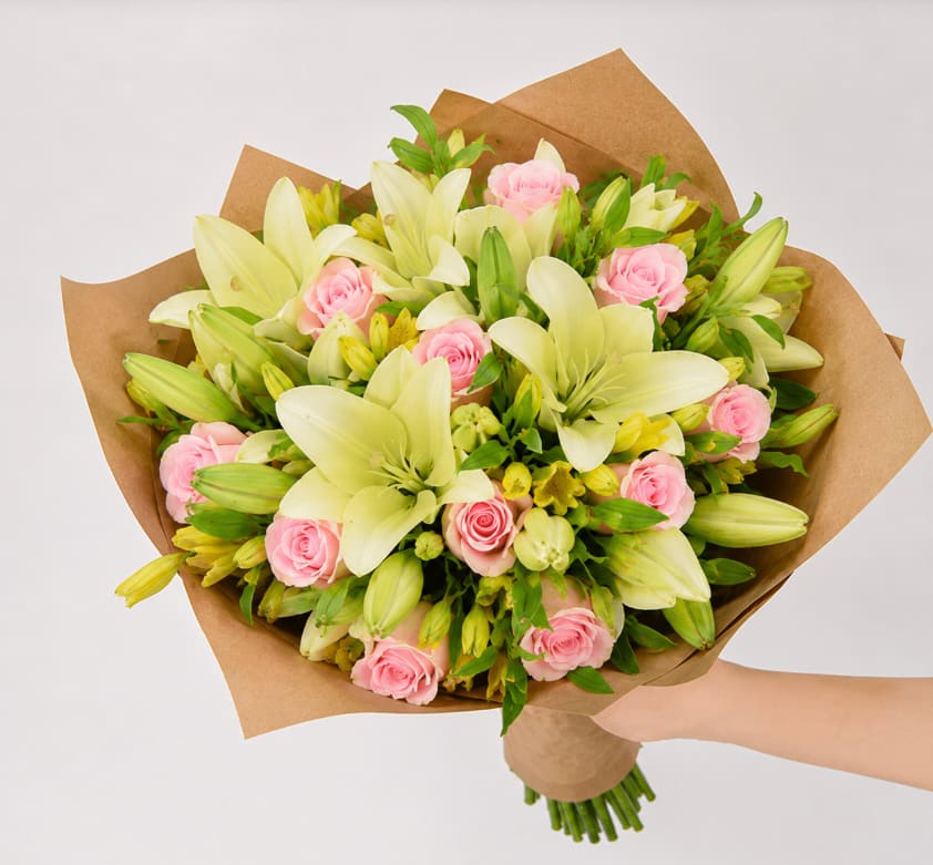 Bouquet of pink roses and pale lilies wrapped in brown paper