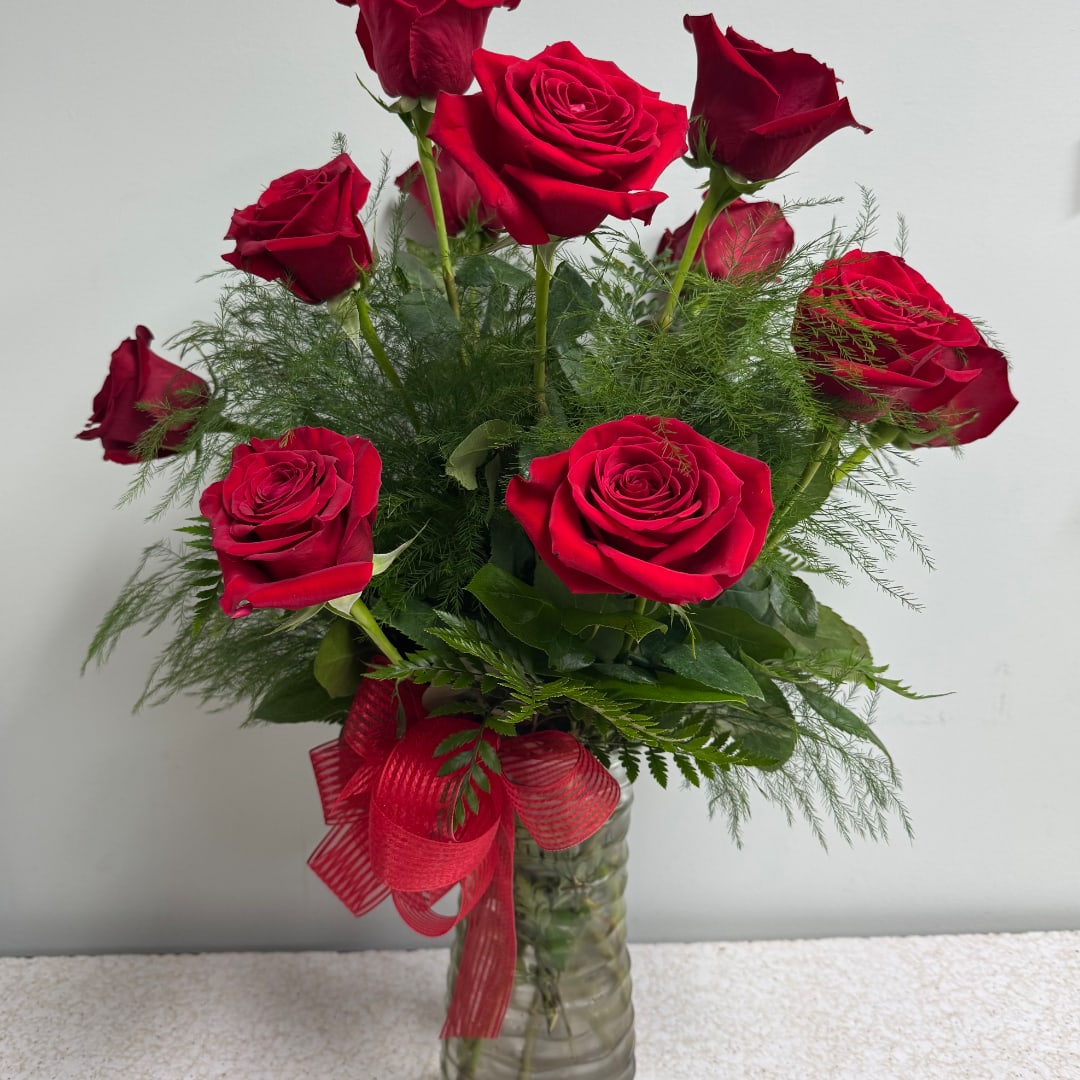 Red roses arranged in a clear glass vase with a red ribbon