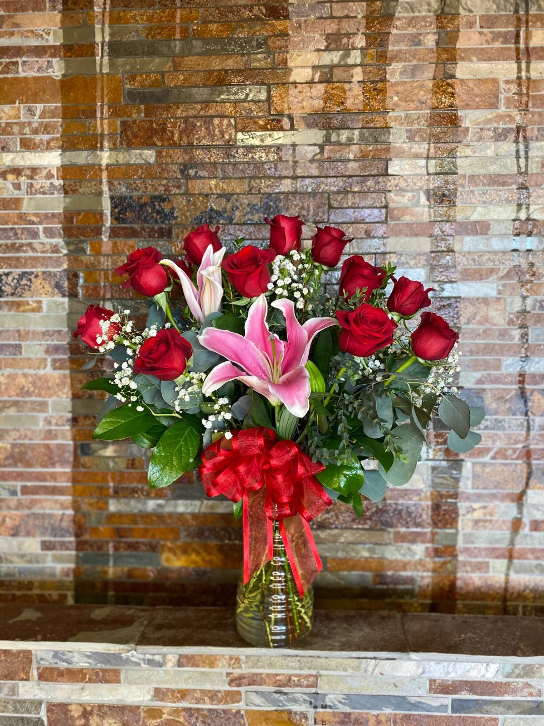 Red roses and pink lilies in a glass vase with a red ribbon