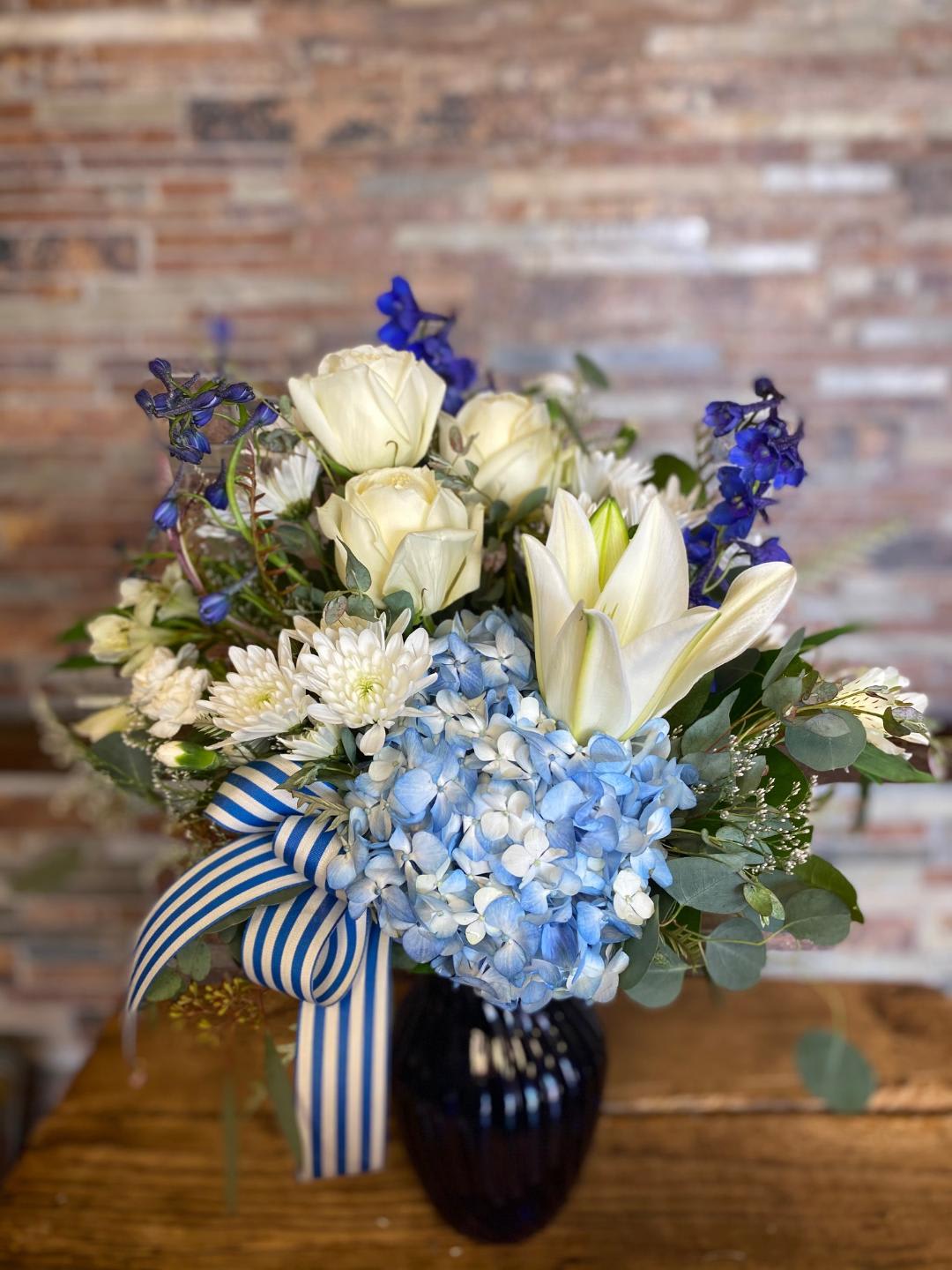 Blue and white bouquet with roses, hydrangeas, lilies, and a striped ribbon in a vase