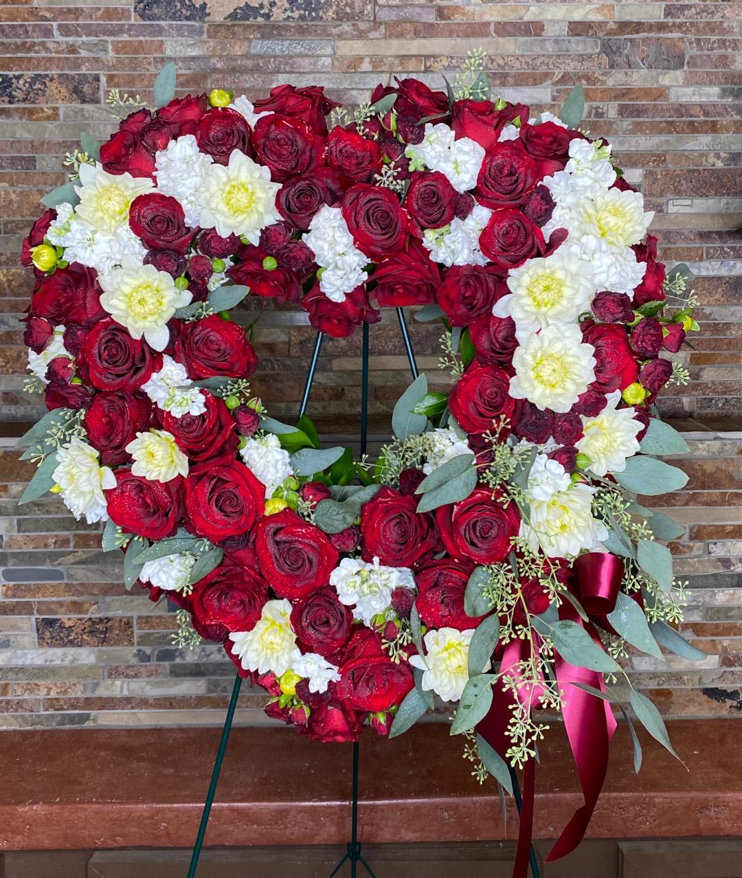 Heart-shaped floral wreath of red roses and white flowers on a stand