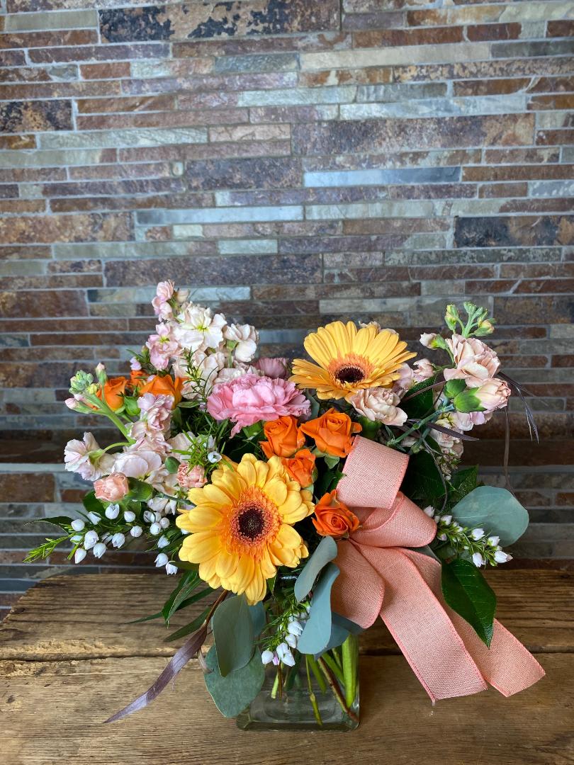 Bouquet of orange roses and yellow gerbera daisies in a glass vase with a pink ribbon