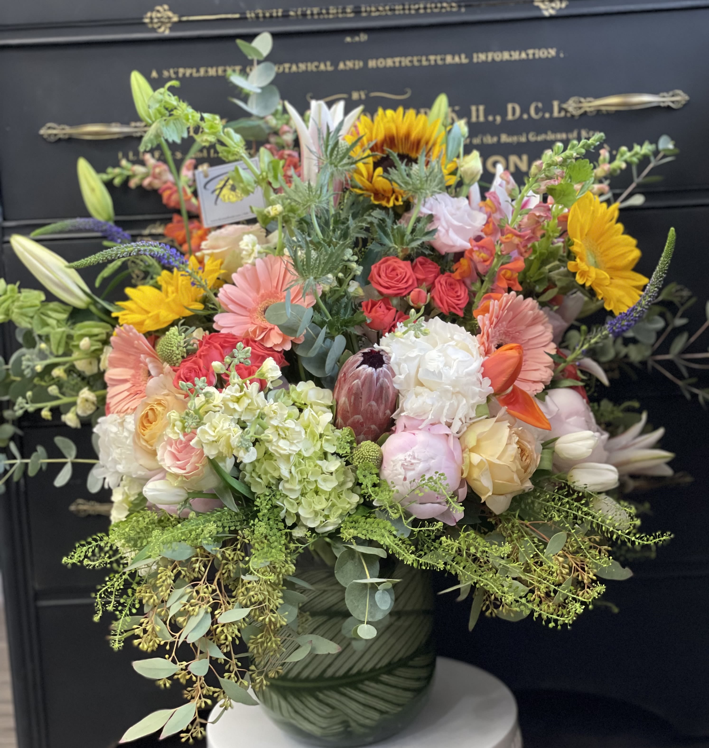 Mixed bouquet in a green patterned vase with sunflowers, roses, and lilies