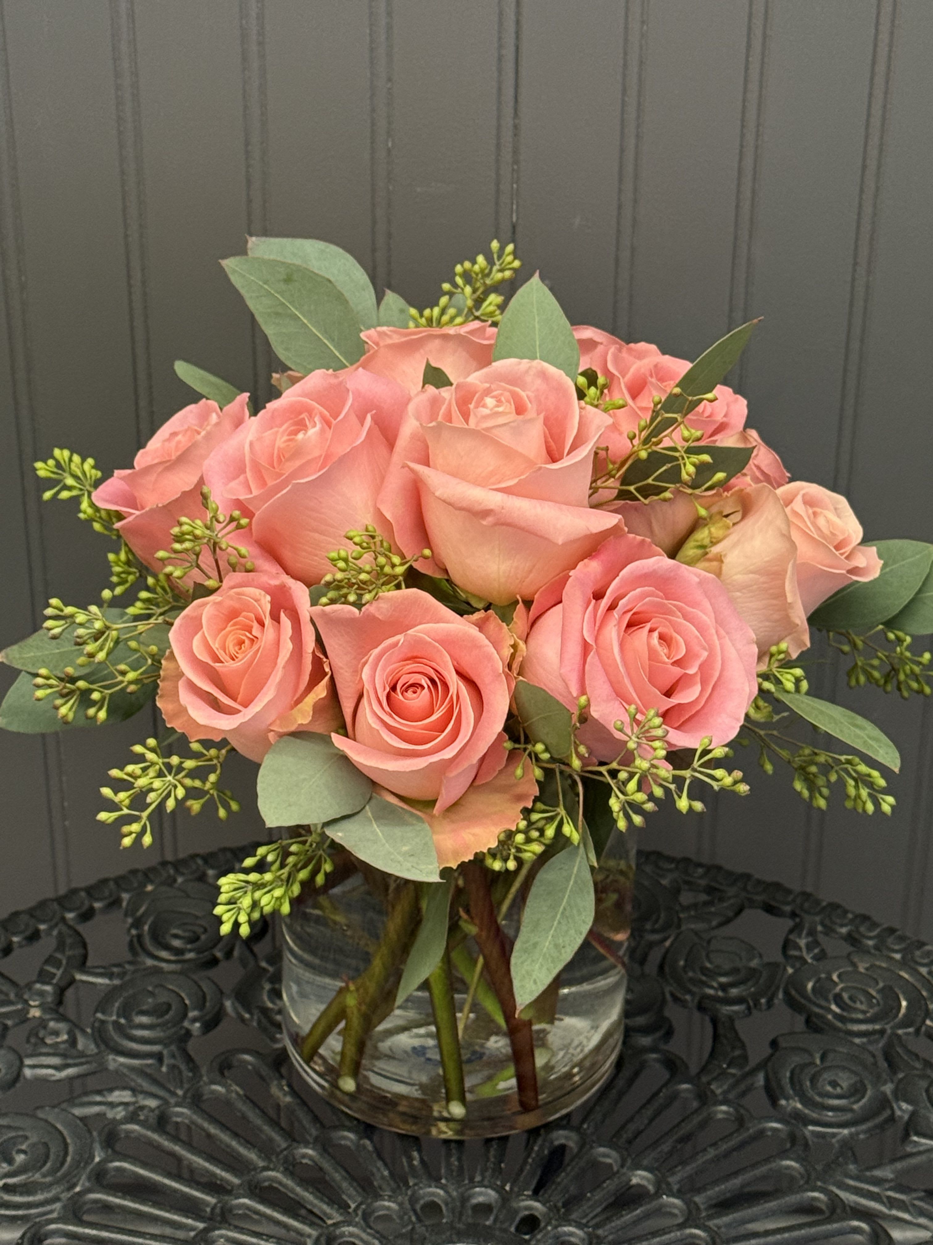 Pink roses arranged in a clear glass vase with greenery