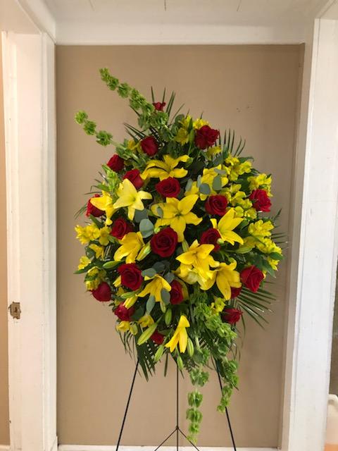 Standing floral spray with red roses and yellow lilies on a metal easel