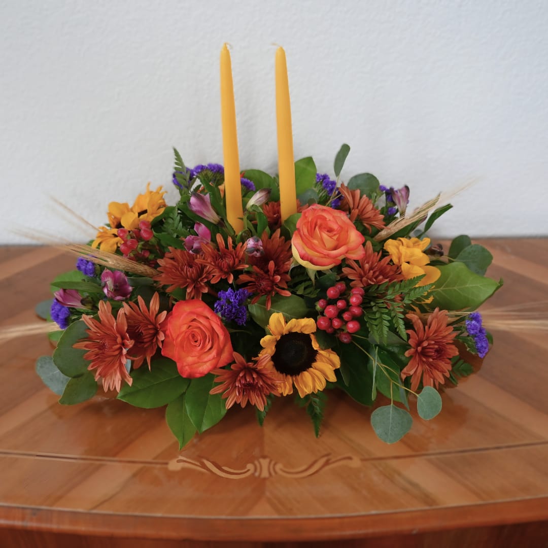Low floral centerpiece with two yellow taper candles and mixed autumn blooms